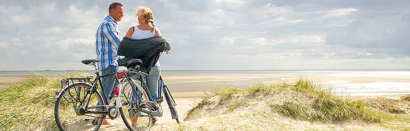 Zwei Fahrradfahrer halten vor eine Düne mit Blick aufs Meer