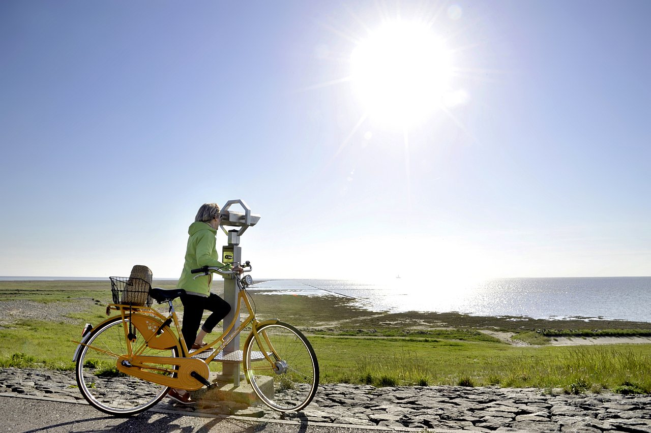 Radfahrerin macht Halt am Ufer und schaut durch ein Teleskop