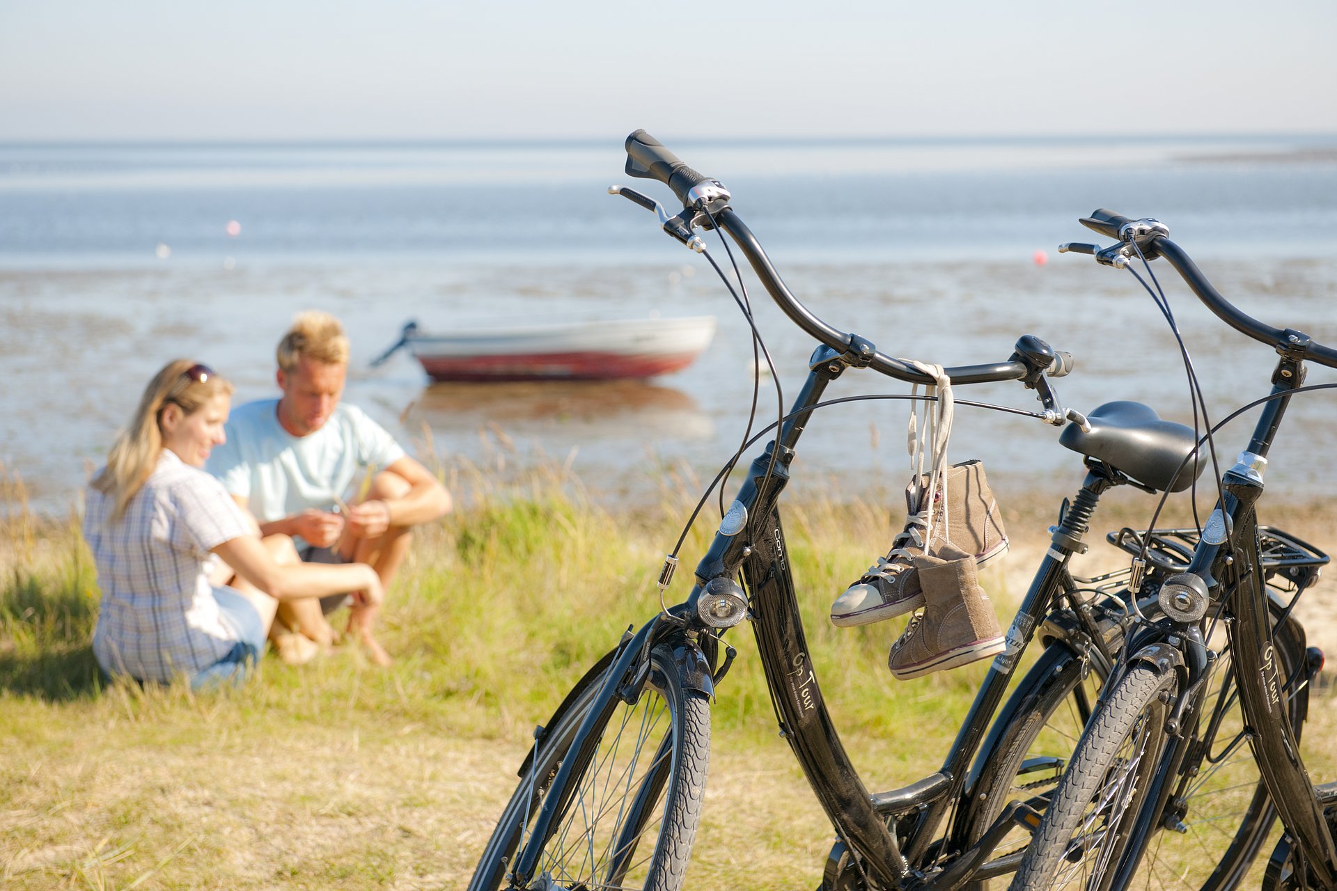 Pärchen sitzt auf Sylt am Strand, ihre Fahrräder im Vordergrund