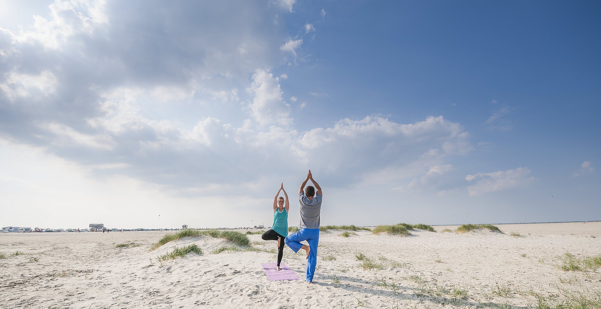 Ein Mann und eine Frau machen Yoga am Strand von St. Peter-Ording.