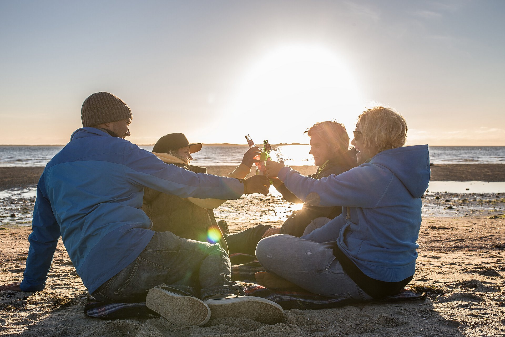 Freunde genießen nach Feierabend den Sonnenuntergang am Föhrer Strand und trinken Deichlimo