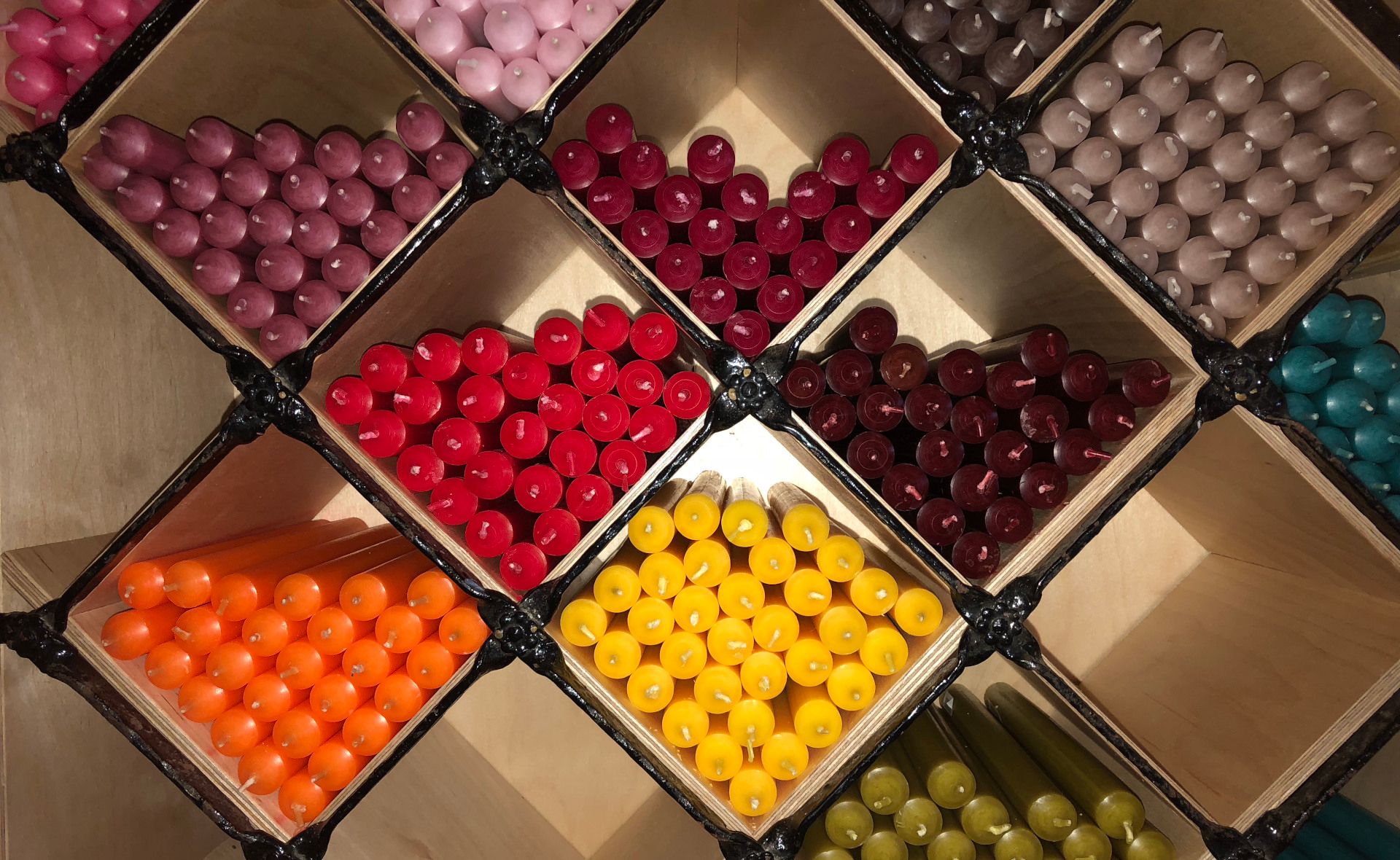 viele Kerzen in verschiedensten Farben liegen in einem Regal in der Kerzen-Diele