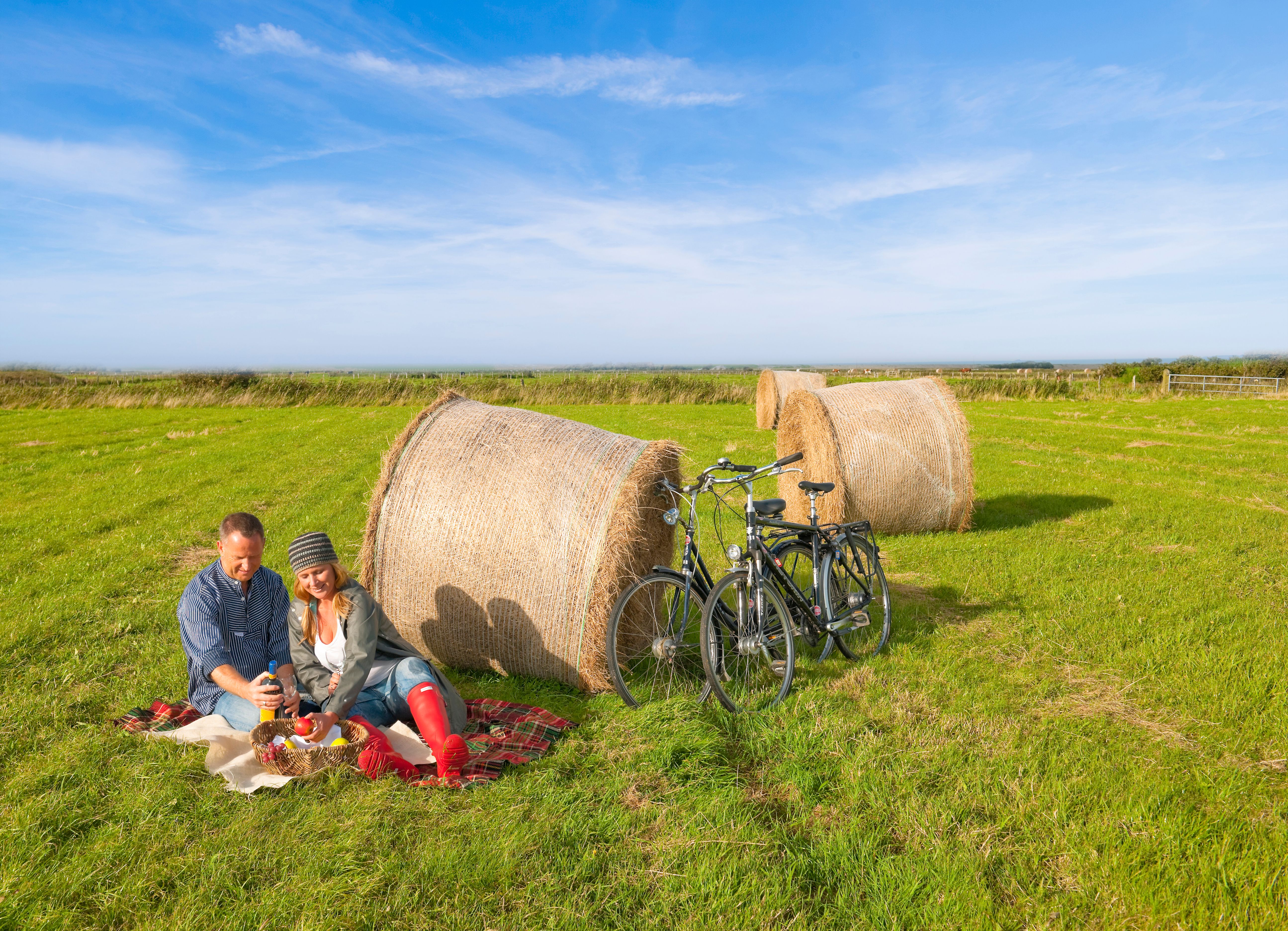 Ein Paar picknickt auf einer Wiese vor großen Heuballen
