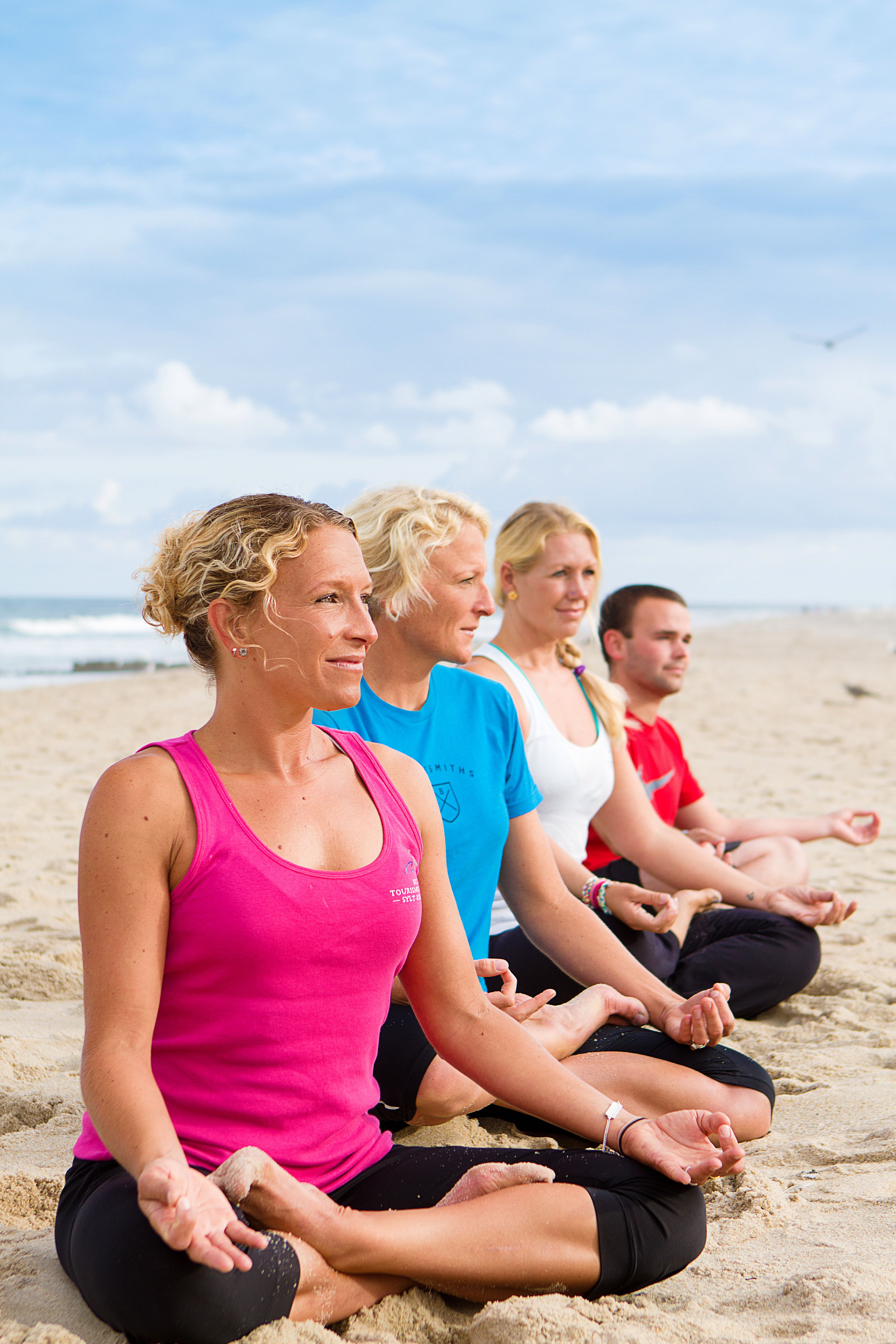 Vier Personen sitzen im Yogi-Sitz am Strand und meditieren