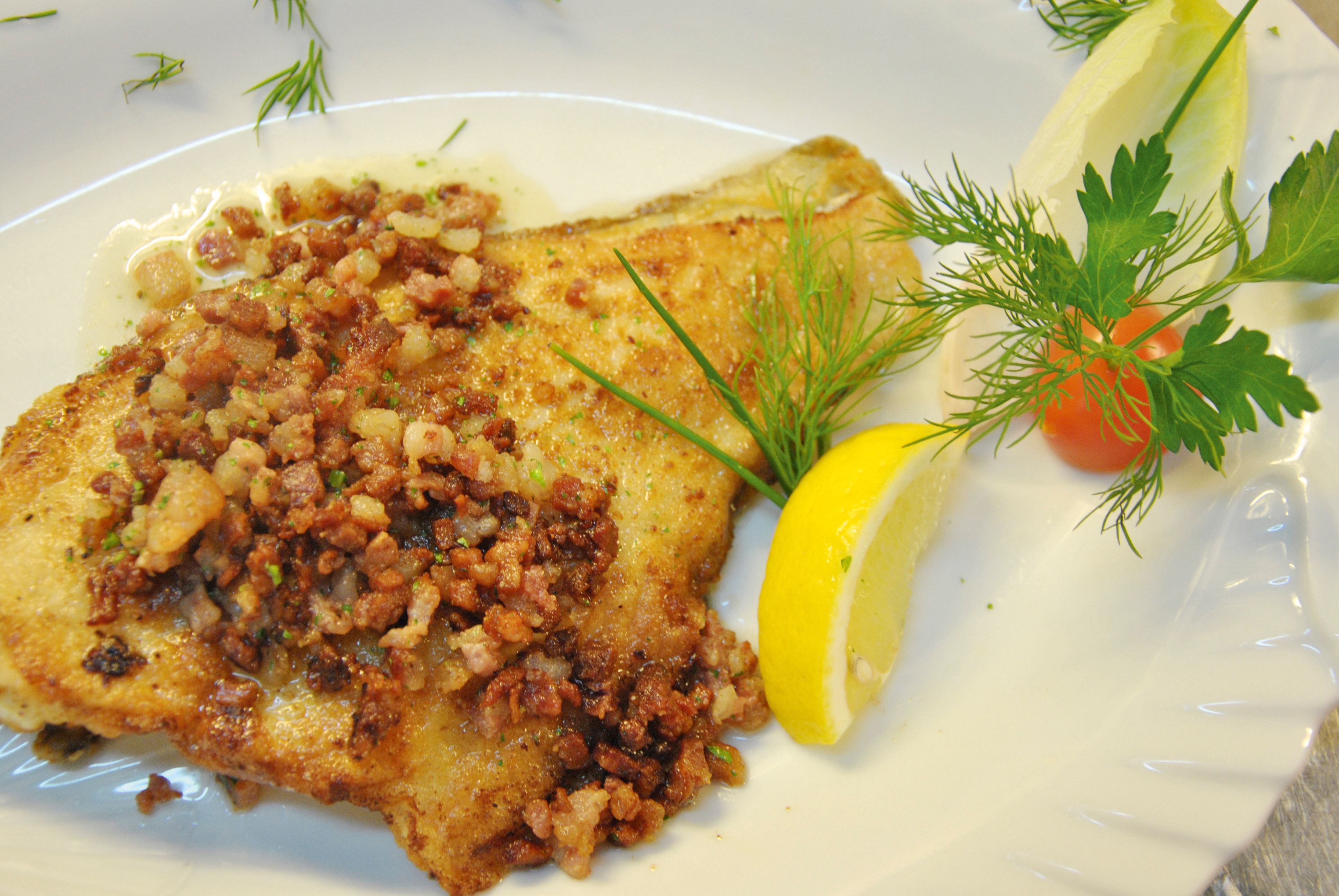 Ein leckeres Schollenfilet mit geröstetem Speck und zerlassener Butter, dekoriert mit Zitrone Dill Tomate und Blattpetersilie. Foto: Föhr Tourismus GmbH/Friedrich Walterscheid