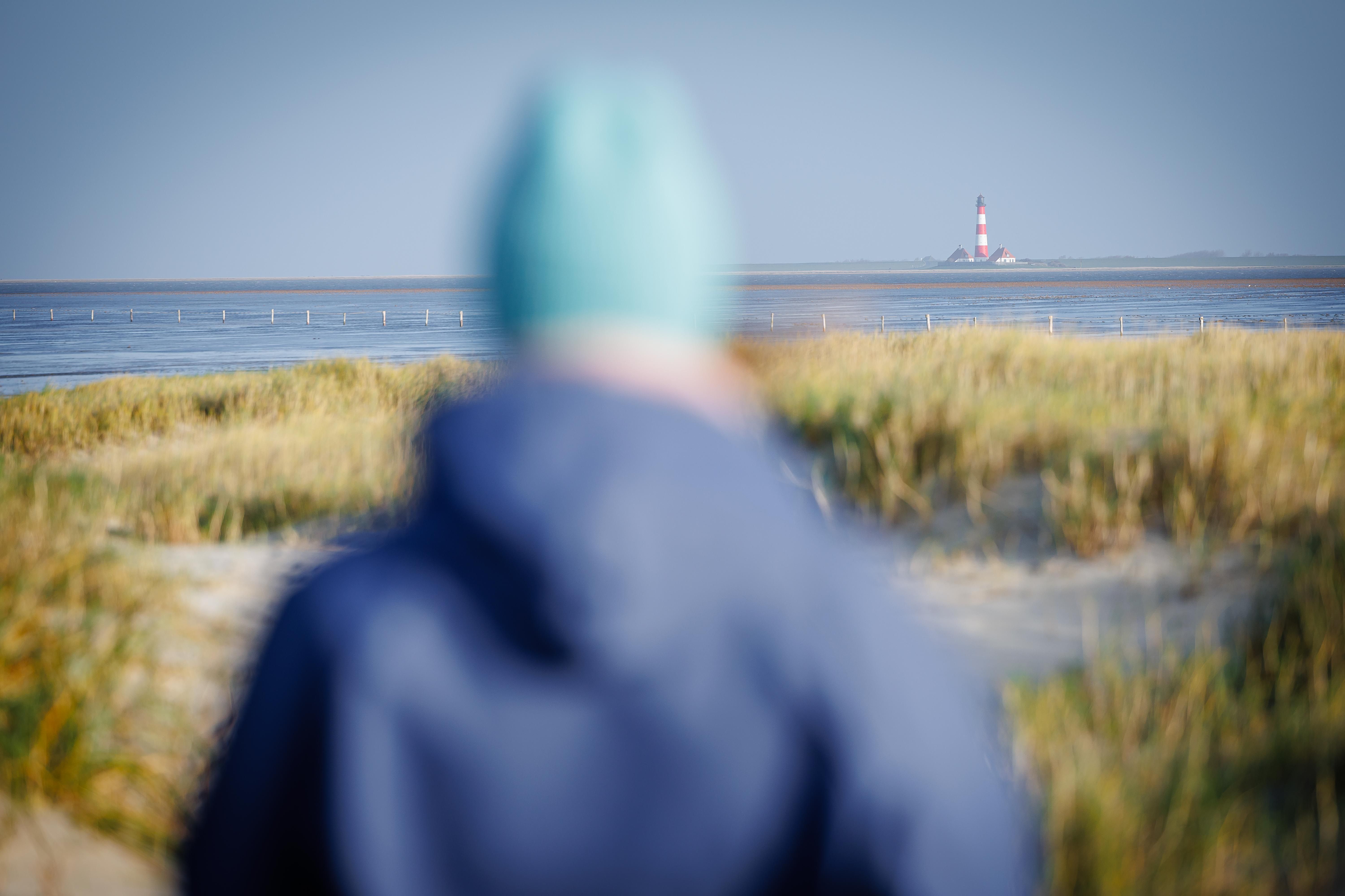 Eine Person steht an den Salzwiesen St. Peter-Ording und schaut auf den Westerhever Leuchtturm