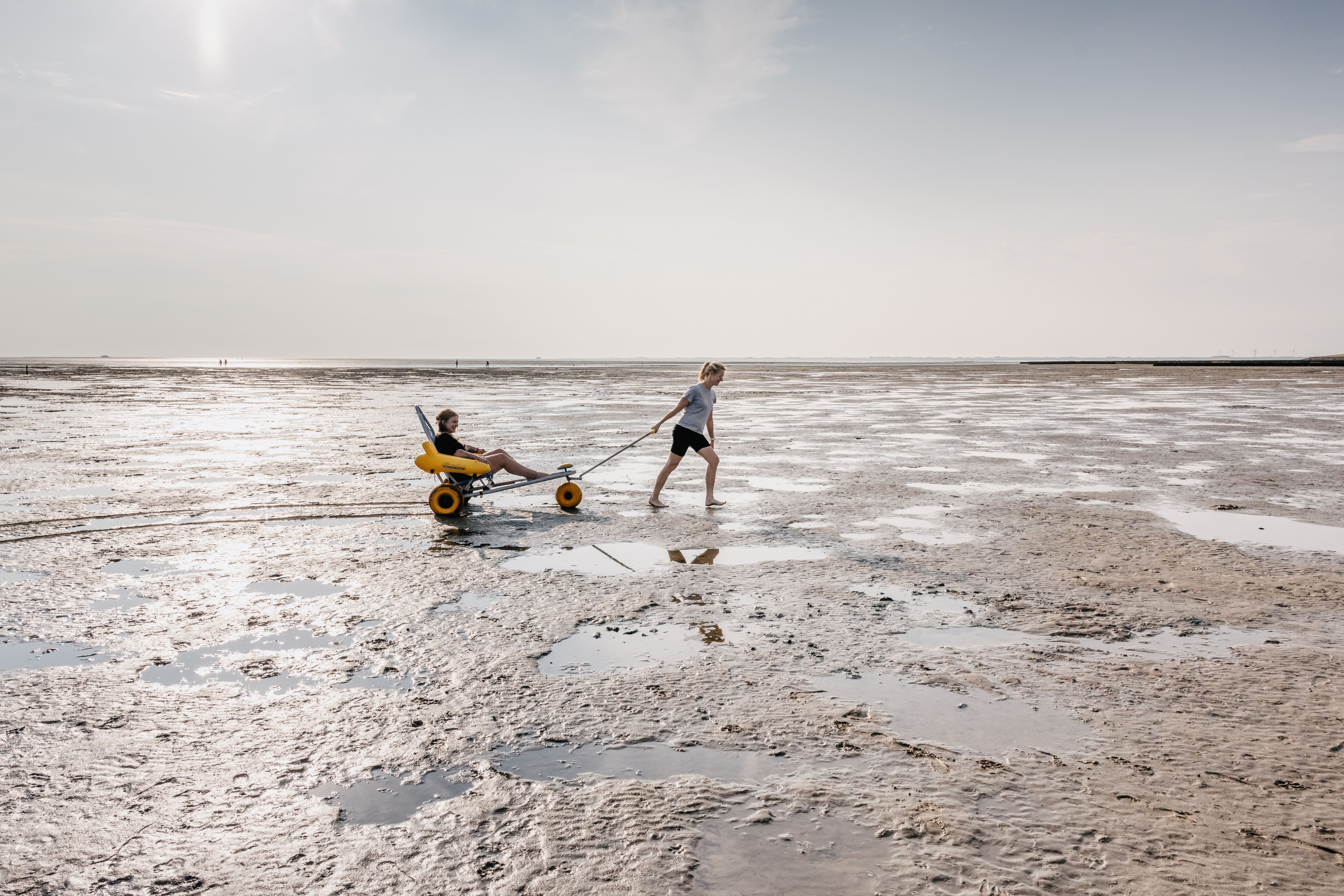 An der Badestelle Fuhlehörn, kann man sich einen Watrollstuhl ausleihen. eine Mitarbeiterin des Tourismusbüros zieht symbolisch eine Kollegin in diesem besonderen Fahrzeug. - Foto: Nordseeküste Nordfriesland Markus Rohrbacher
