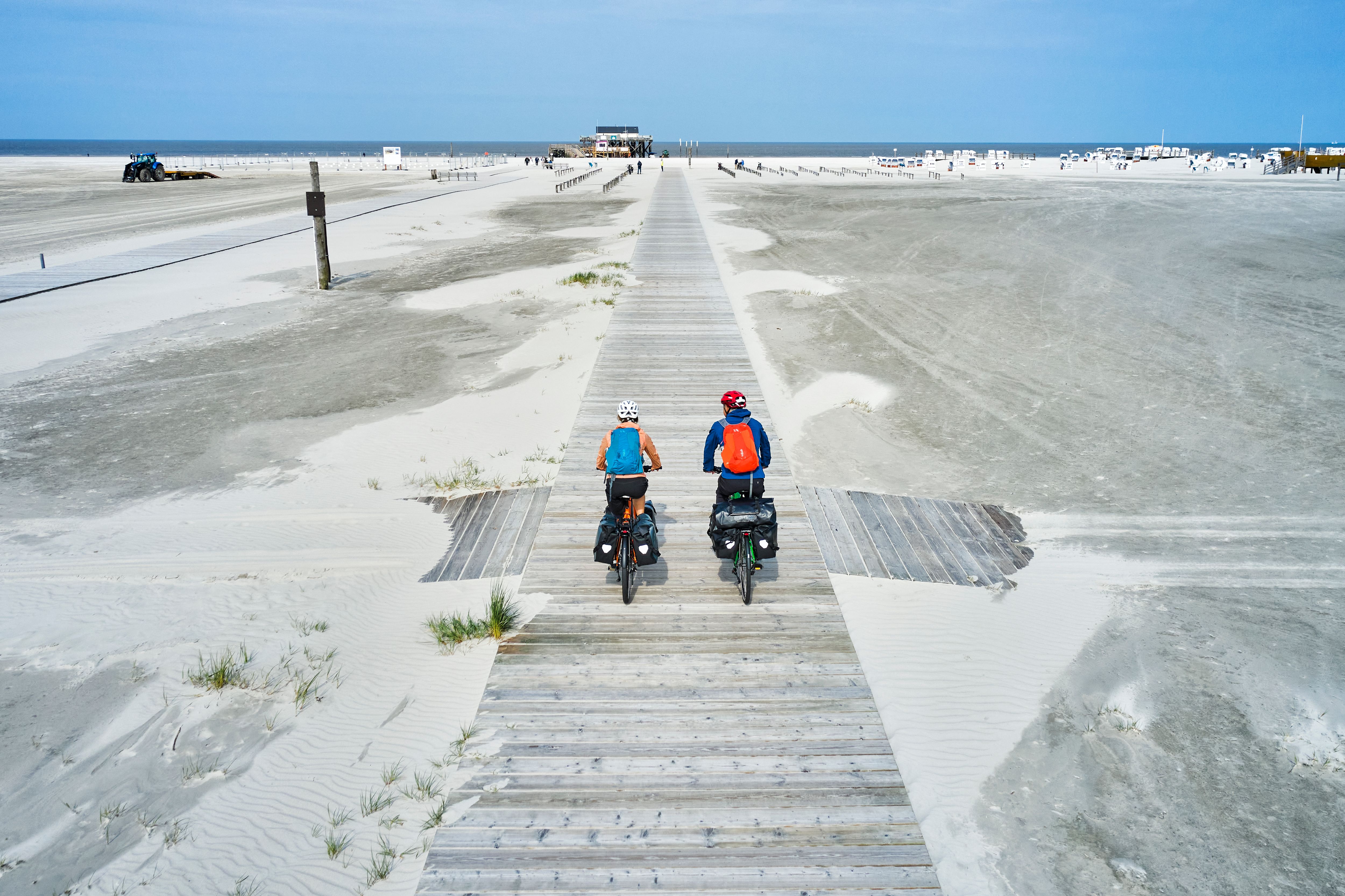 Zwei Radfahrer fahren am Strand von St. Peter-Ording entlang