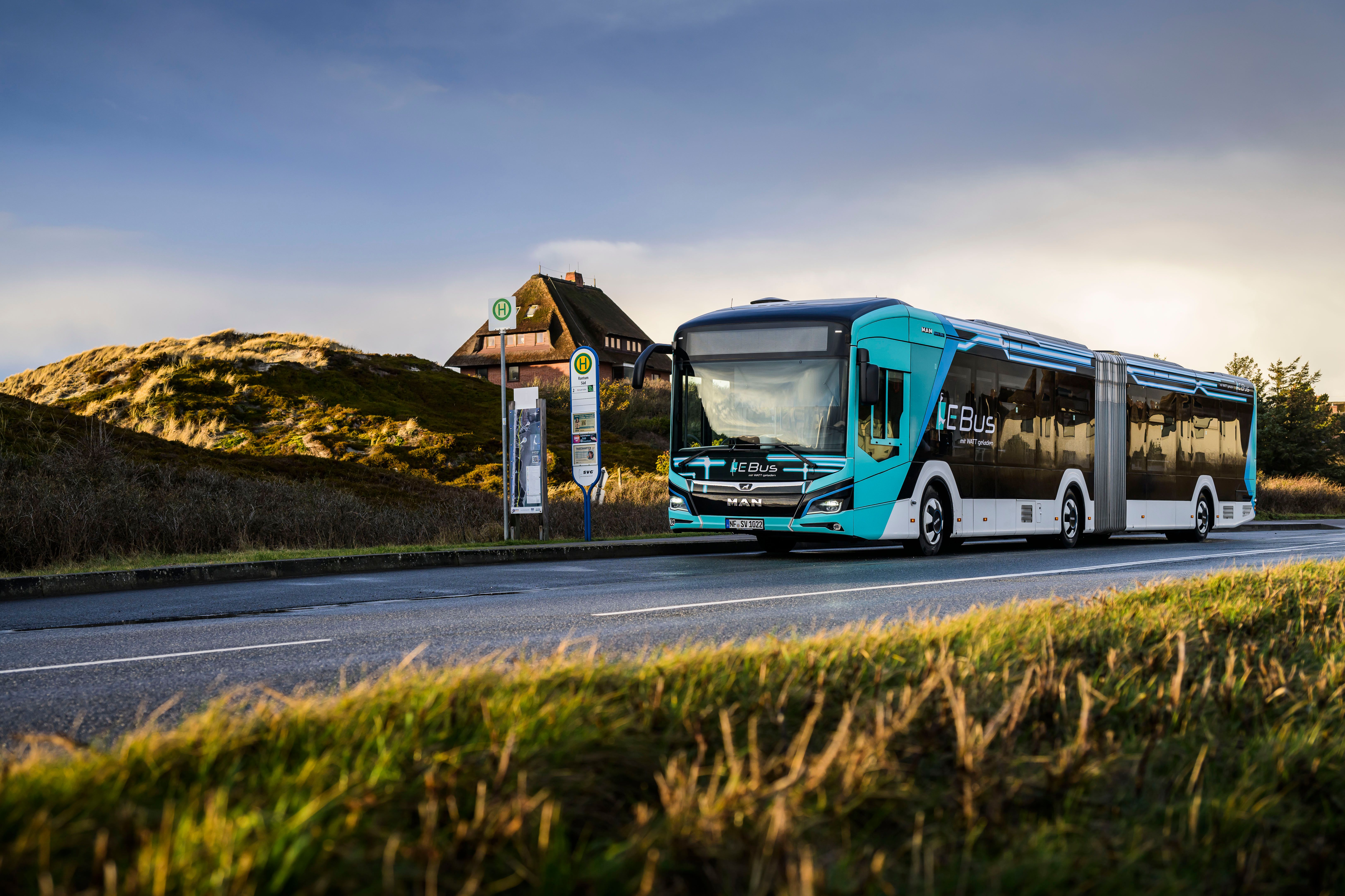 Ein neuer Gelenkbuss der Sylter Verkehrsbetriebe in Cyanblau mit Weiß und dunklen Fenstern steht an einer Bushaltestelle auf Sylt.