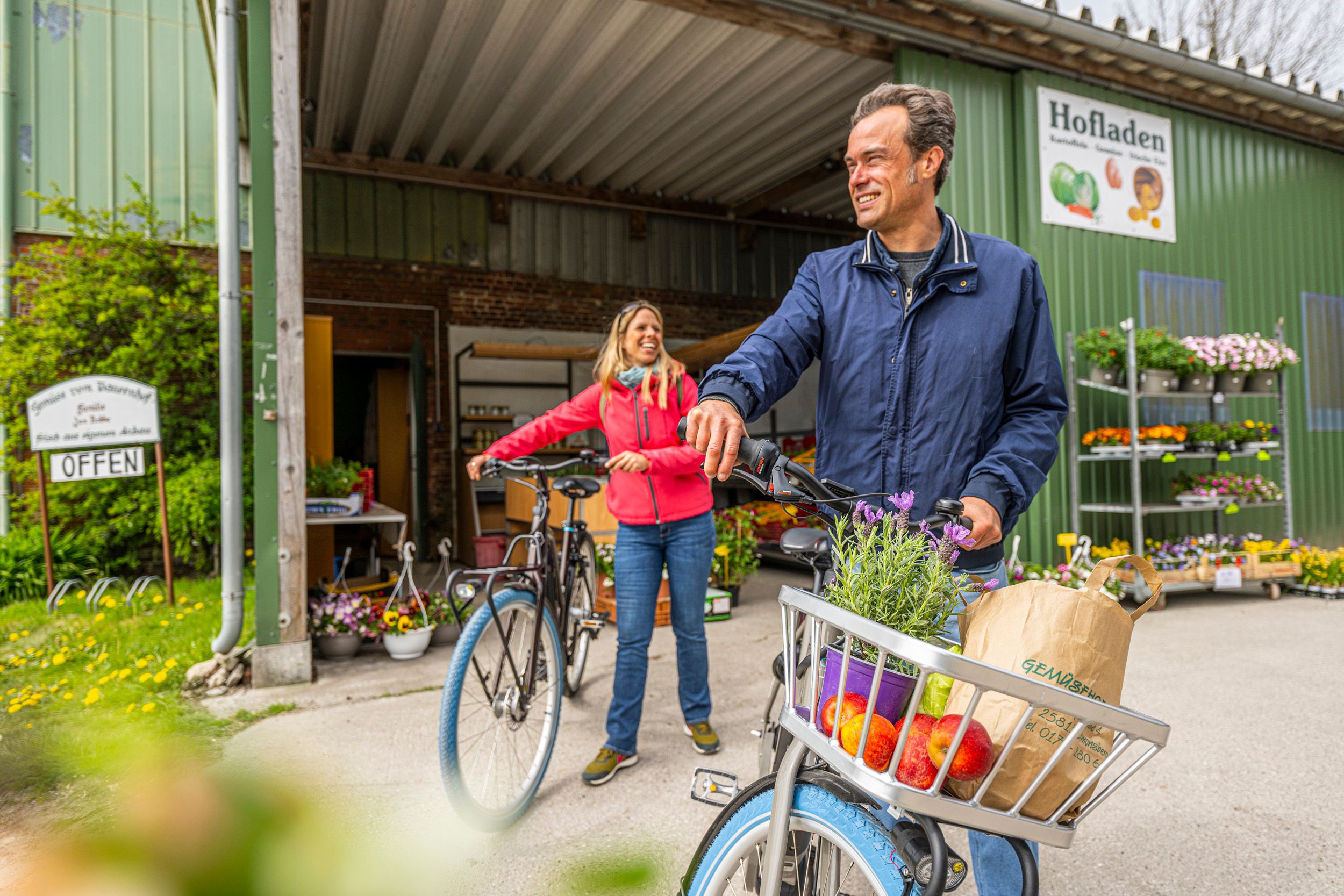 Zwei Radfahrer halten vor einem Hofladen, in dem sie viel eingekauft haben