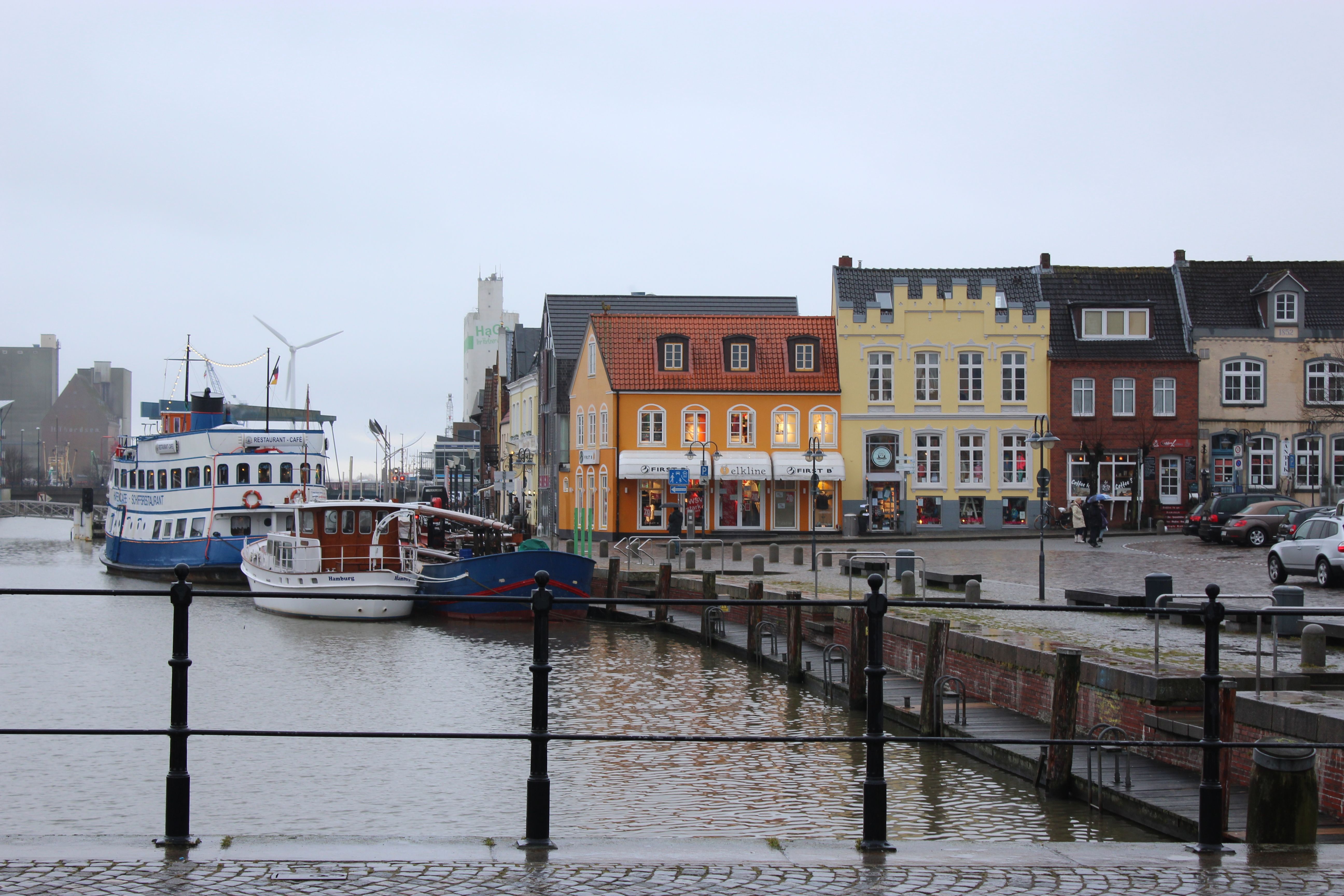 Blick auf den die bunten Häuser am Husumer Hafen, an der Kaimauer liegen mehrere Schiffe