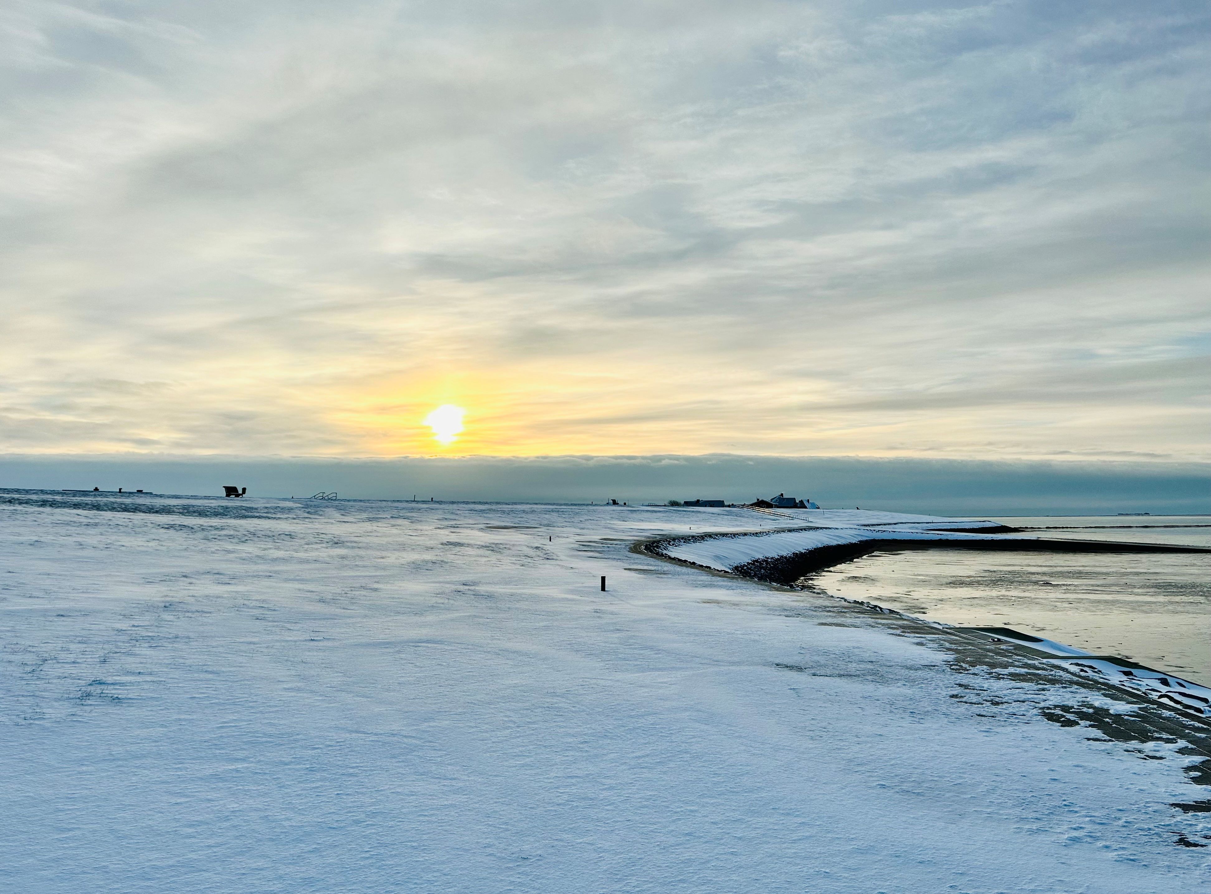 Verschneiter Deich von Dagebüll bei tiefstehender Sonne. Es ist ein windstiller Tag, der Schnee liegt sanft da. 