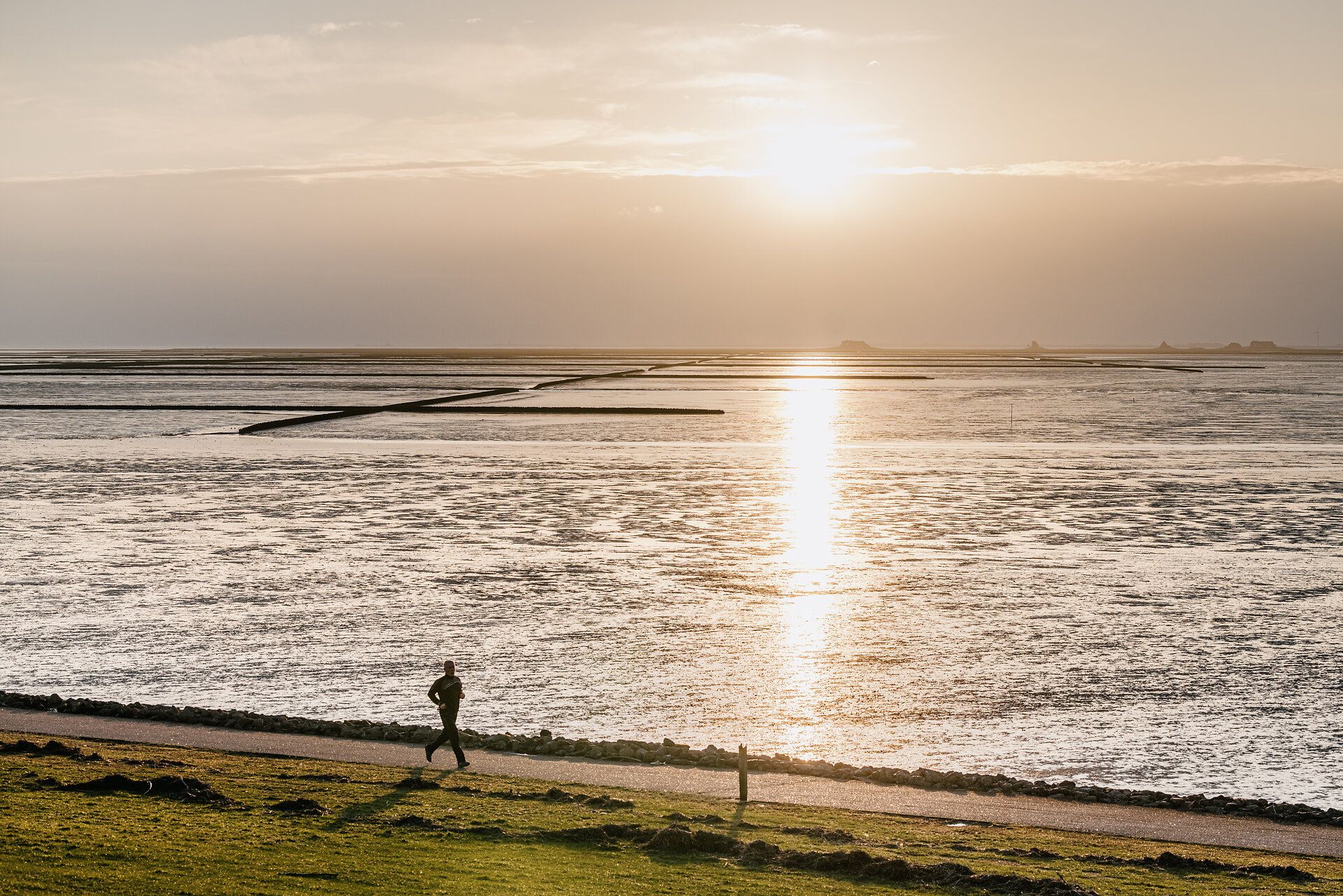 Ein Läufer joggt im Sonnenuntergang am Strand Lüttmoorsiel entlang