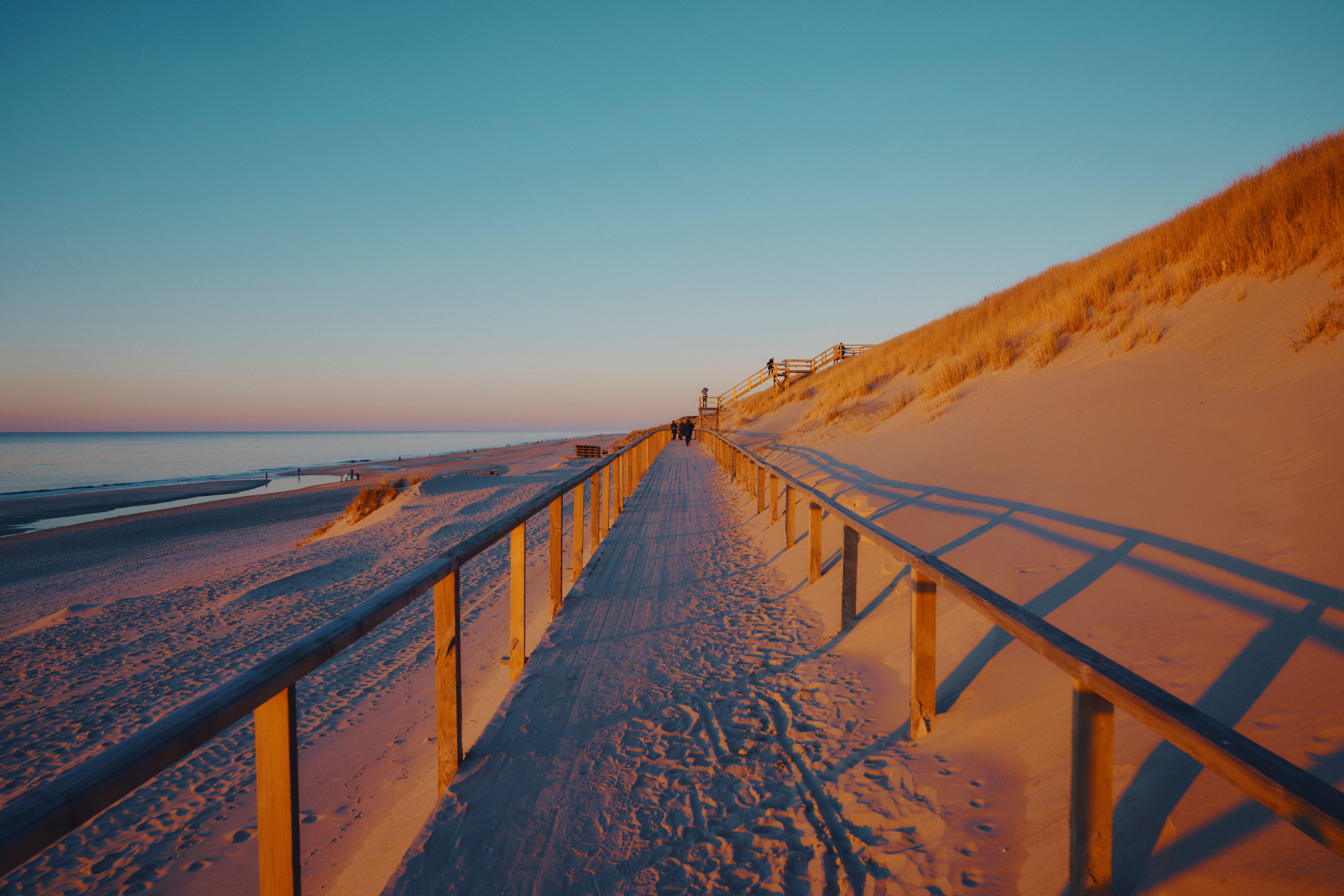 Der Dünensteg auf Sylt bei Winter im Abendlicht. Links ist das Meer, rechts die Dünen zu sehen.