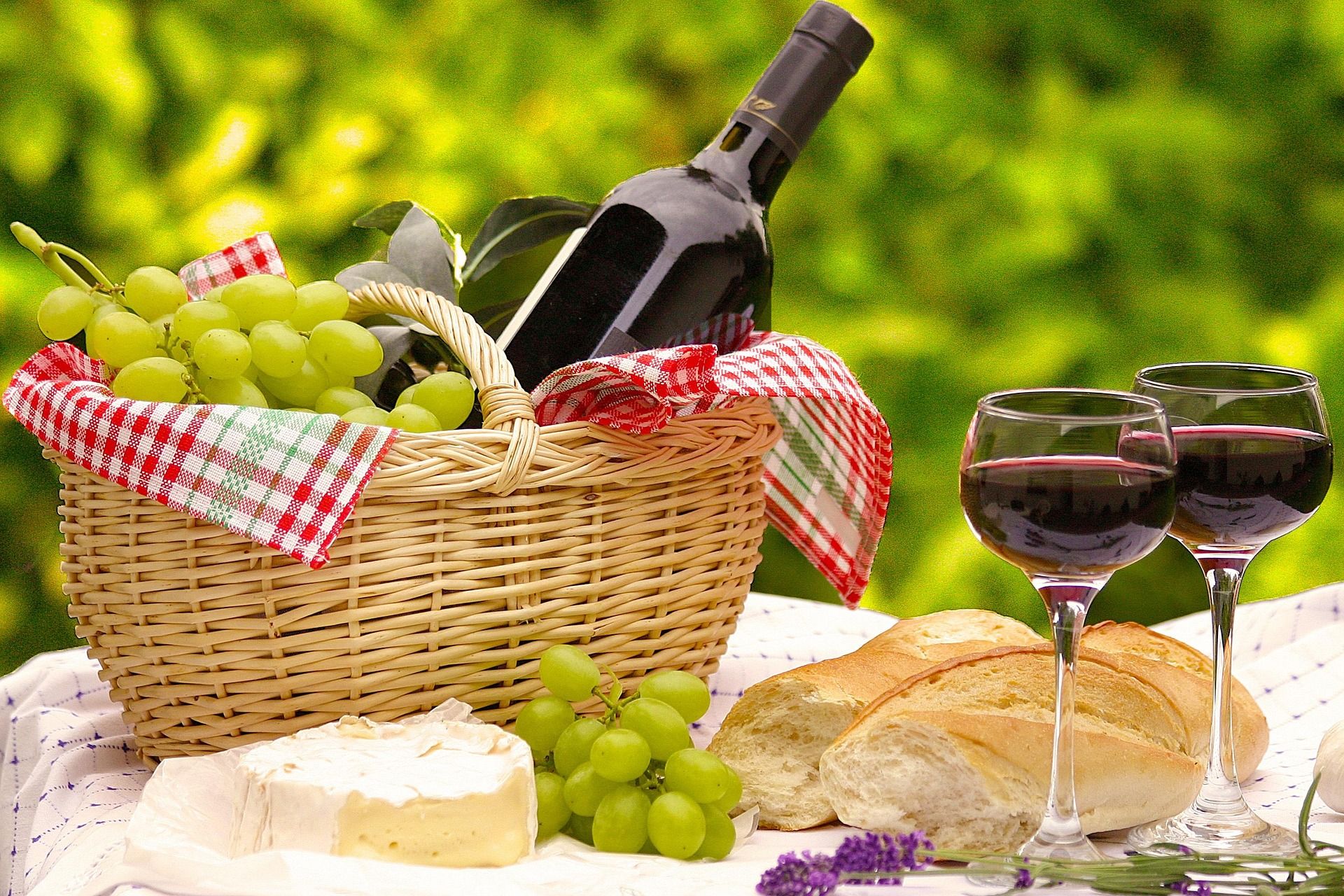 gefüllter Picknickkorb, davor stehen zwei Gläser mit Wein