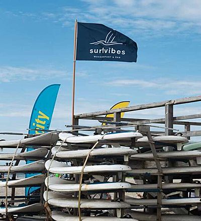 Gestapelte Surfbretter der Surfschule surfvibes mit der Fahne des neuen Unternehmens. Foto: surfvibes
