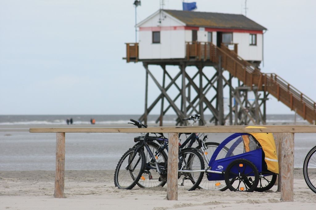 Fahrräder stehen am Strand von St. Peter-Ording, im Hintergrund ein Pfahlbau