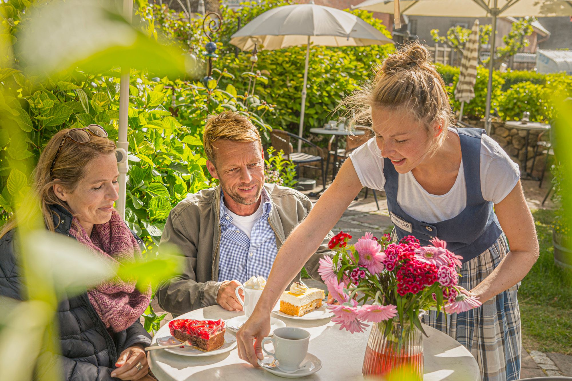 Gäste sitzen auf der Terrasse des Friesen-Cafés und bekommen gerade von der Bedienung Kaffee und Kuchen