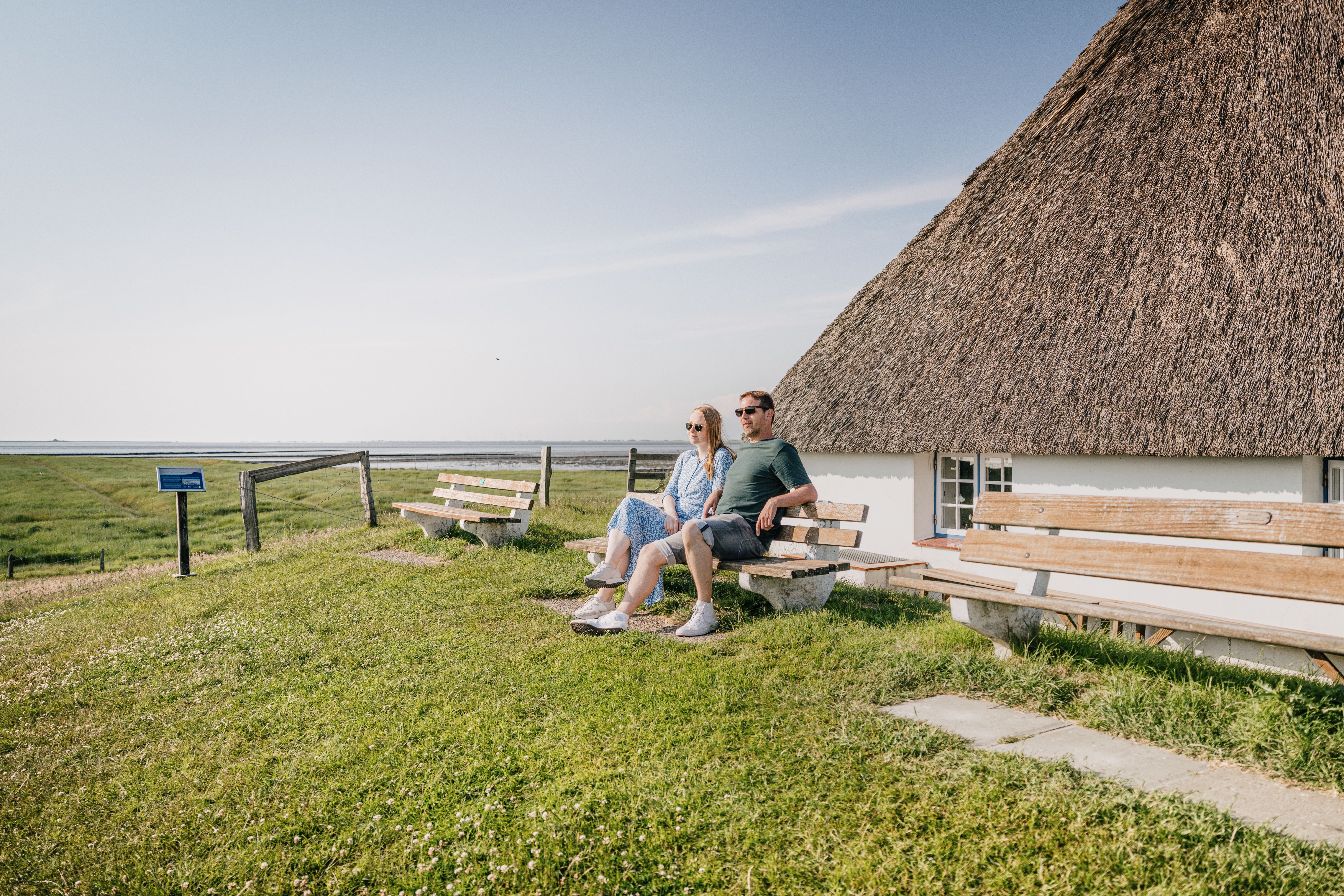 Ein paar sitzt in der Sonne auf einer Bank vor dem Hallig Krog