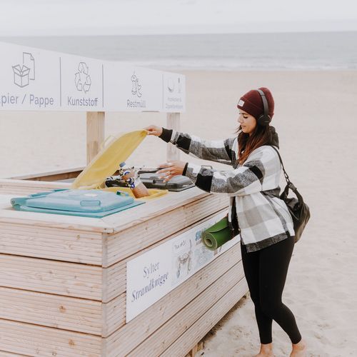 Am Strand entsorgt wirft eine Frau Müll in einen großen Strandmülleimer