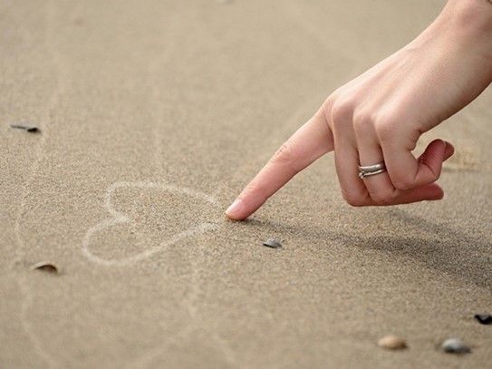 Jemand malt mit dem Zeigefinger ein Herz in den Sand