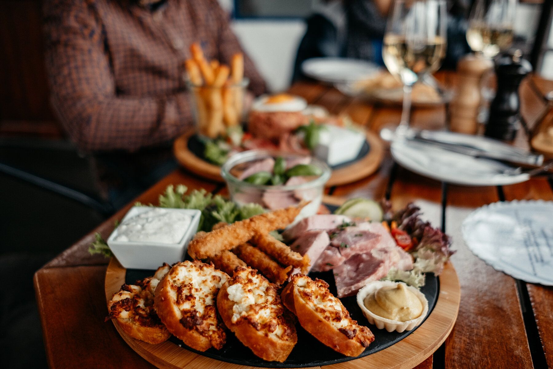 Der Blick geht auf einen Tisch mit mehreren ala Tappas angerichteten Tellern mit Fingerfood, im Hintergrund kann man noch erahnen, das zwei Personen sitzen.