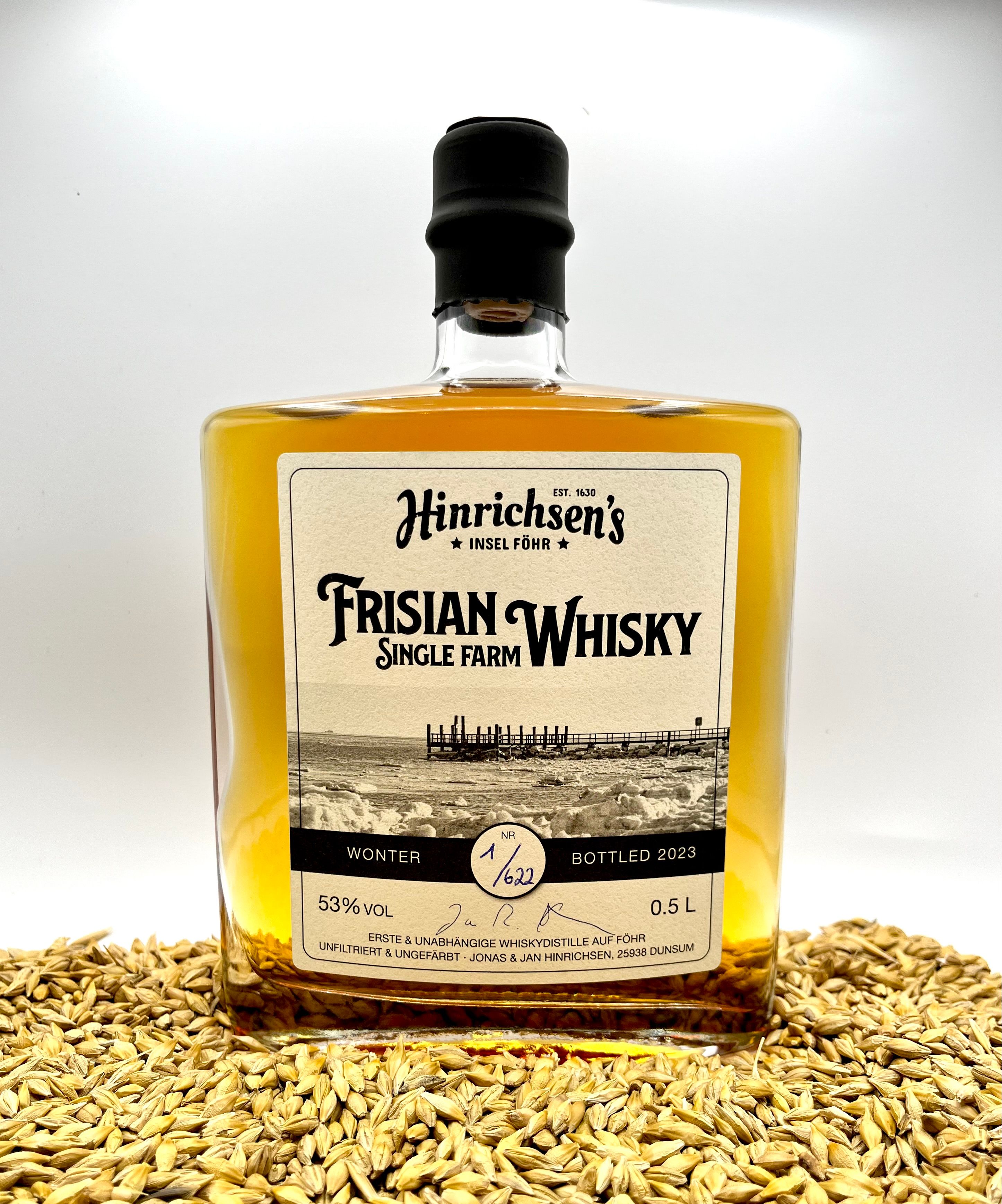 Eine Whyski Flasche "Hinrichsens Frisian Whisky" steht auf einem kleinen Haufen Gerstenkörner. Foto: Hinrichsen Farm