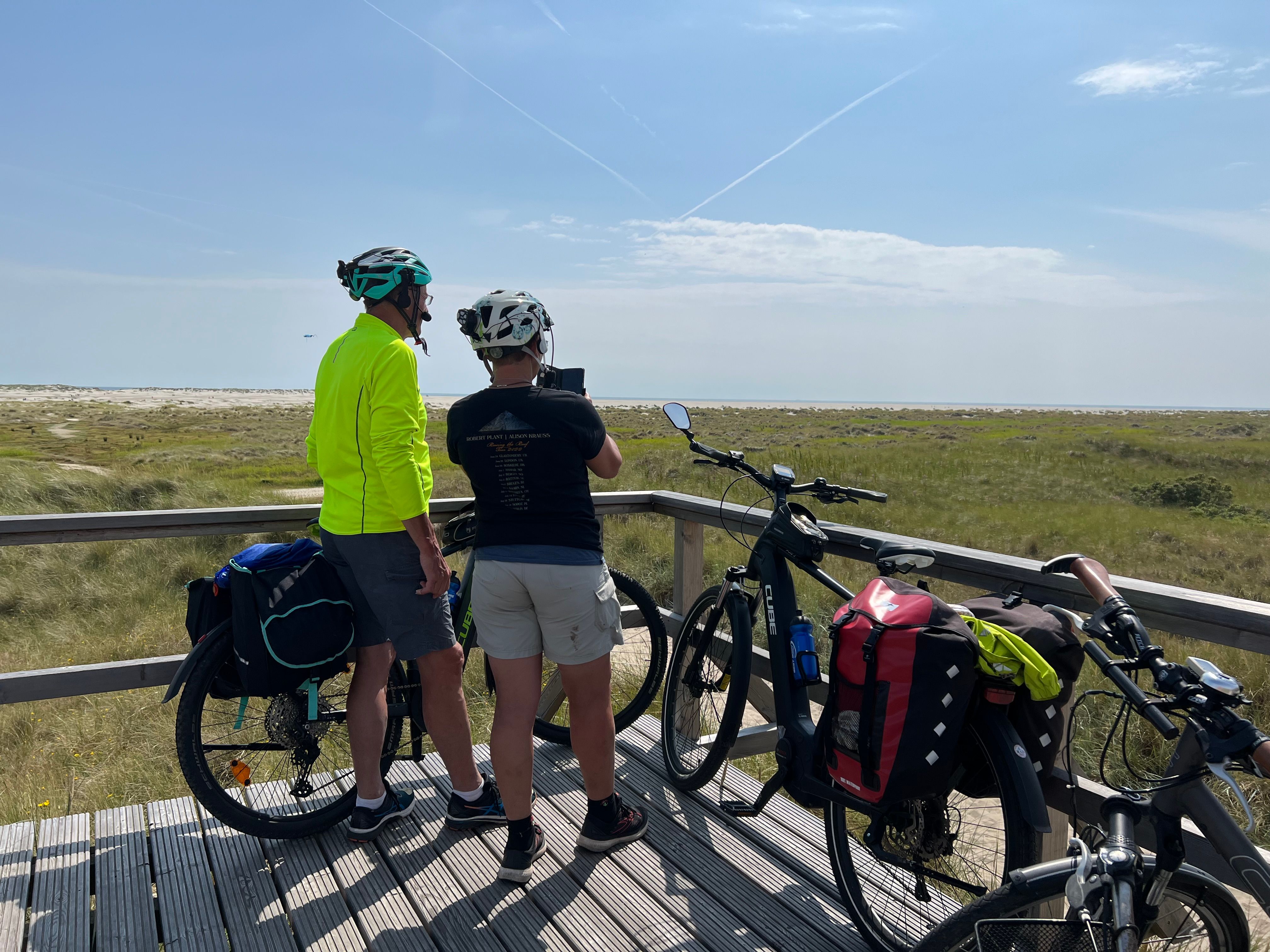Zwei Radfahrer stehen auf einem Ausblickspunkt inmitten der Dünen von Amrum und blicken in die Weite