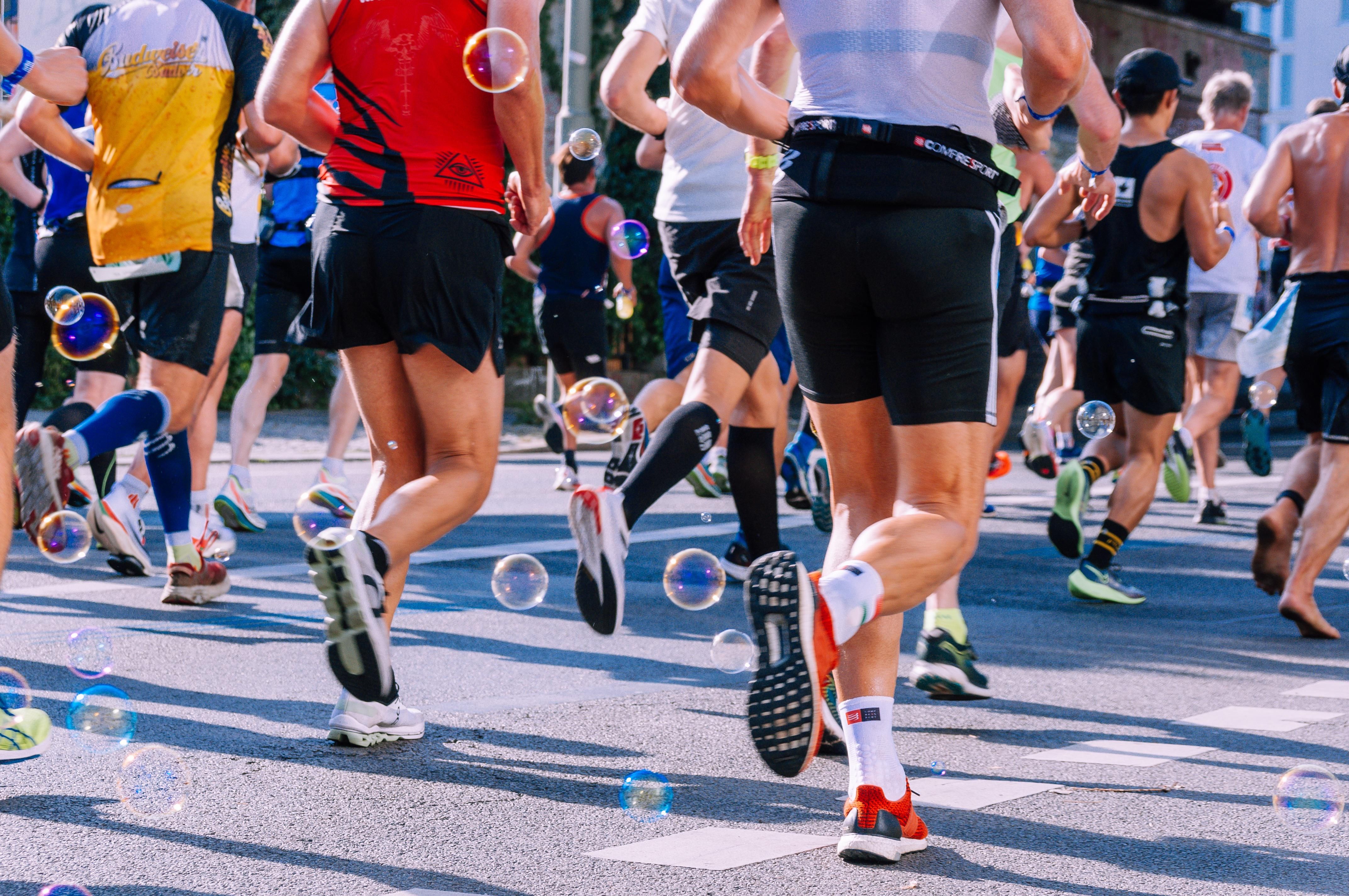 Läufer laufen bei einem Marathon mit, zwischen ihren Bienen fliegen Seifenblasen