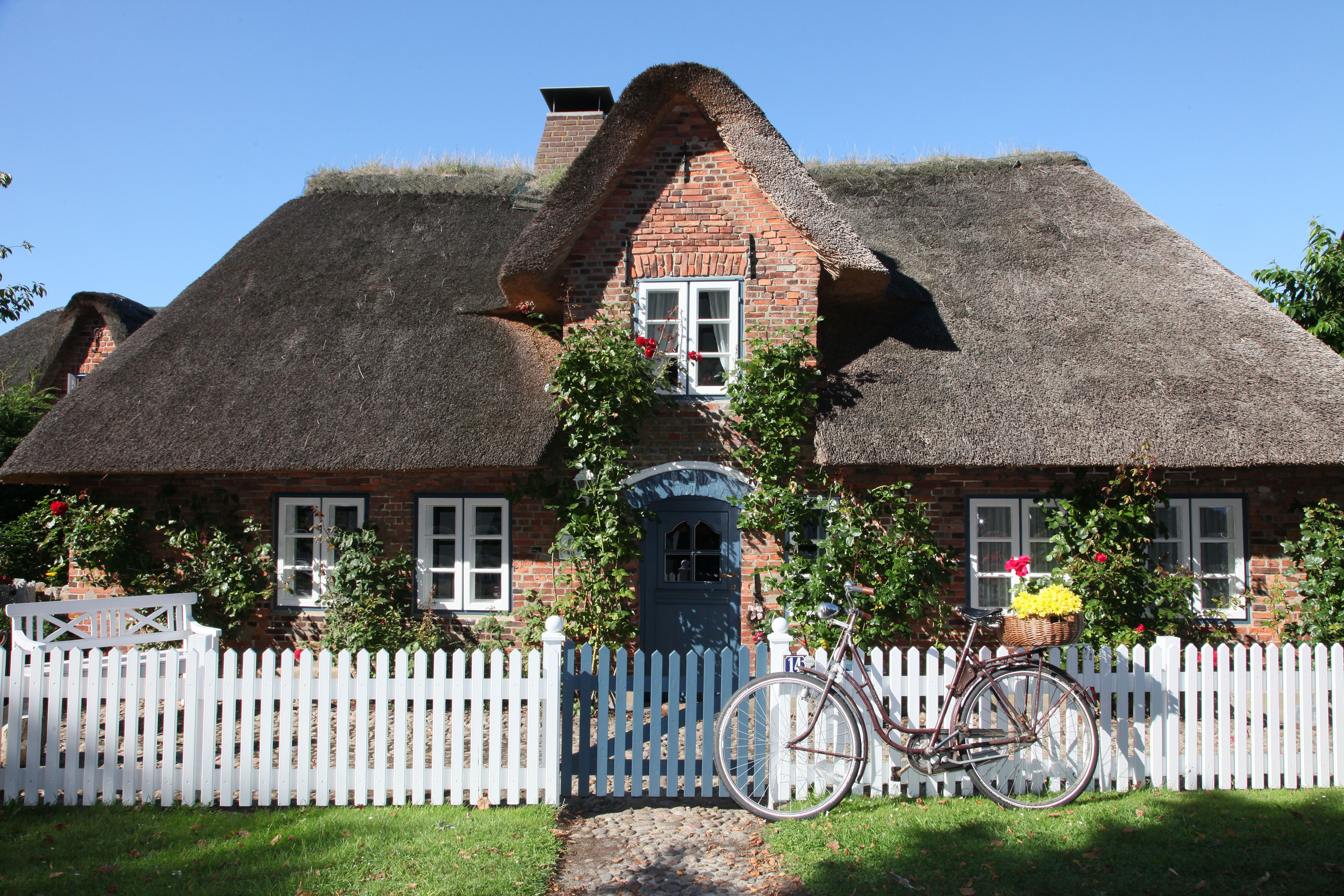 eine typische Friesenkate, reetgedeckt und mit weißem Holzzaun und Zaunpforte. Foto: Föhr Tourismus GmbH | Folke Winkelmann