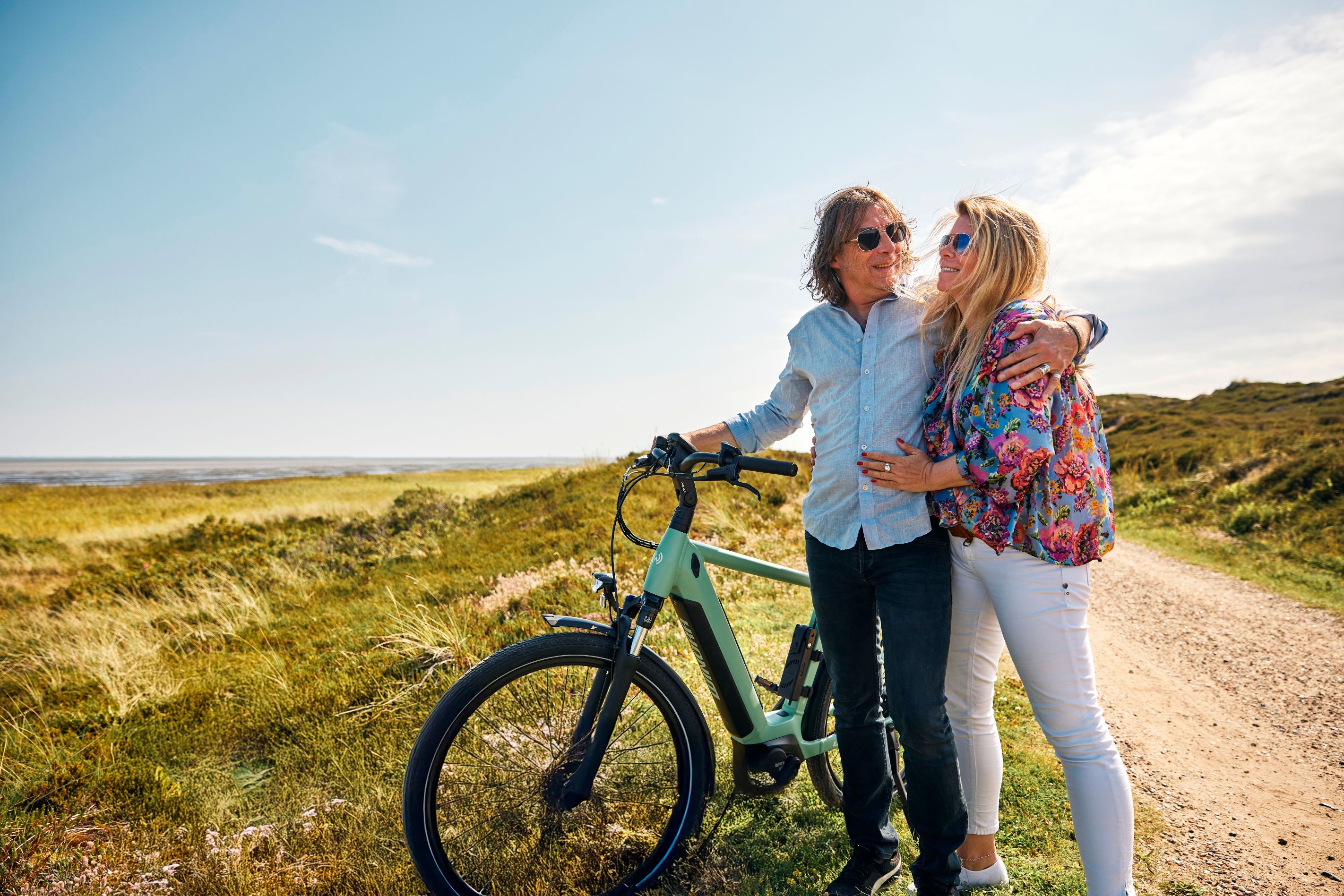 Ein älteres Paar steht eingehackt mit einem Mountenbike in den Dünen an einem Sandschotterweg. Foto: Lars Jockumsen