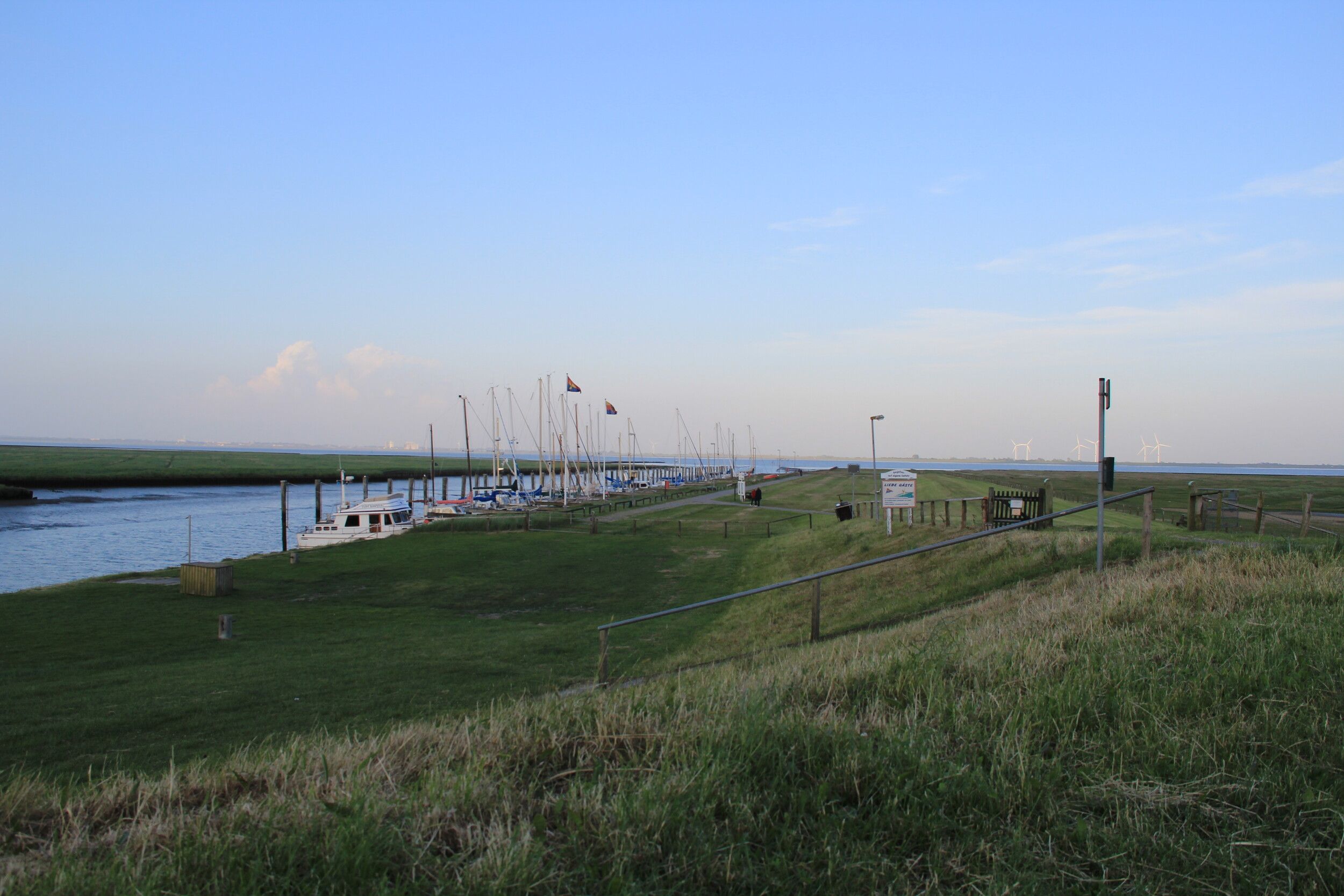 Blick vom Deich, im Hintergrund liegen einige Schiffe in einem kleinen Hafen