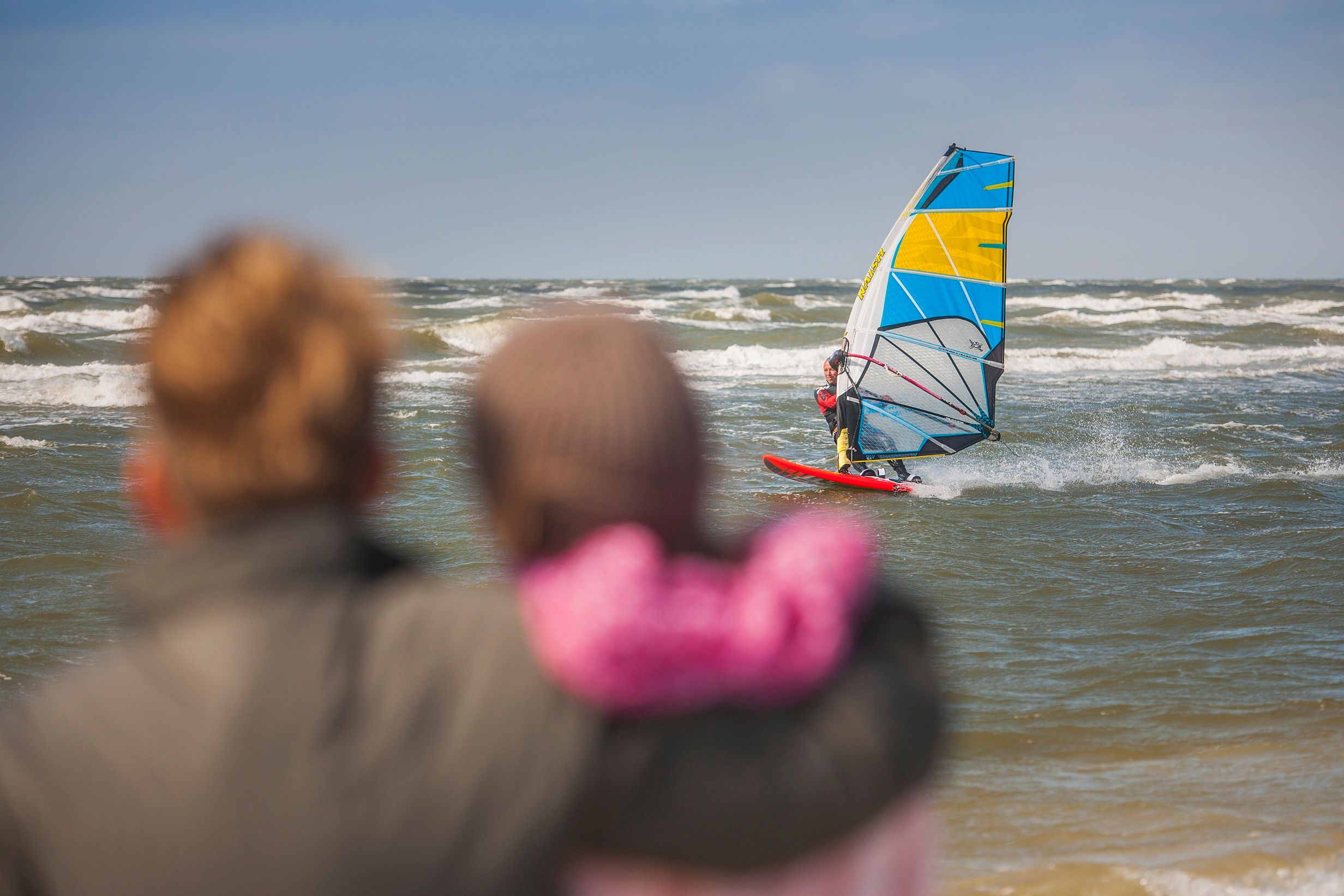 Ein Pärchen schaut am Strand von St. Peter-Ording einem Windsurfer beim Surfen zu. Foto: Oliver Franke