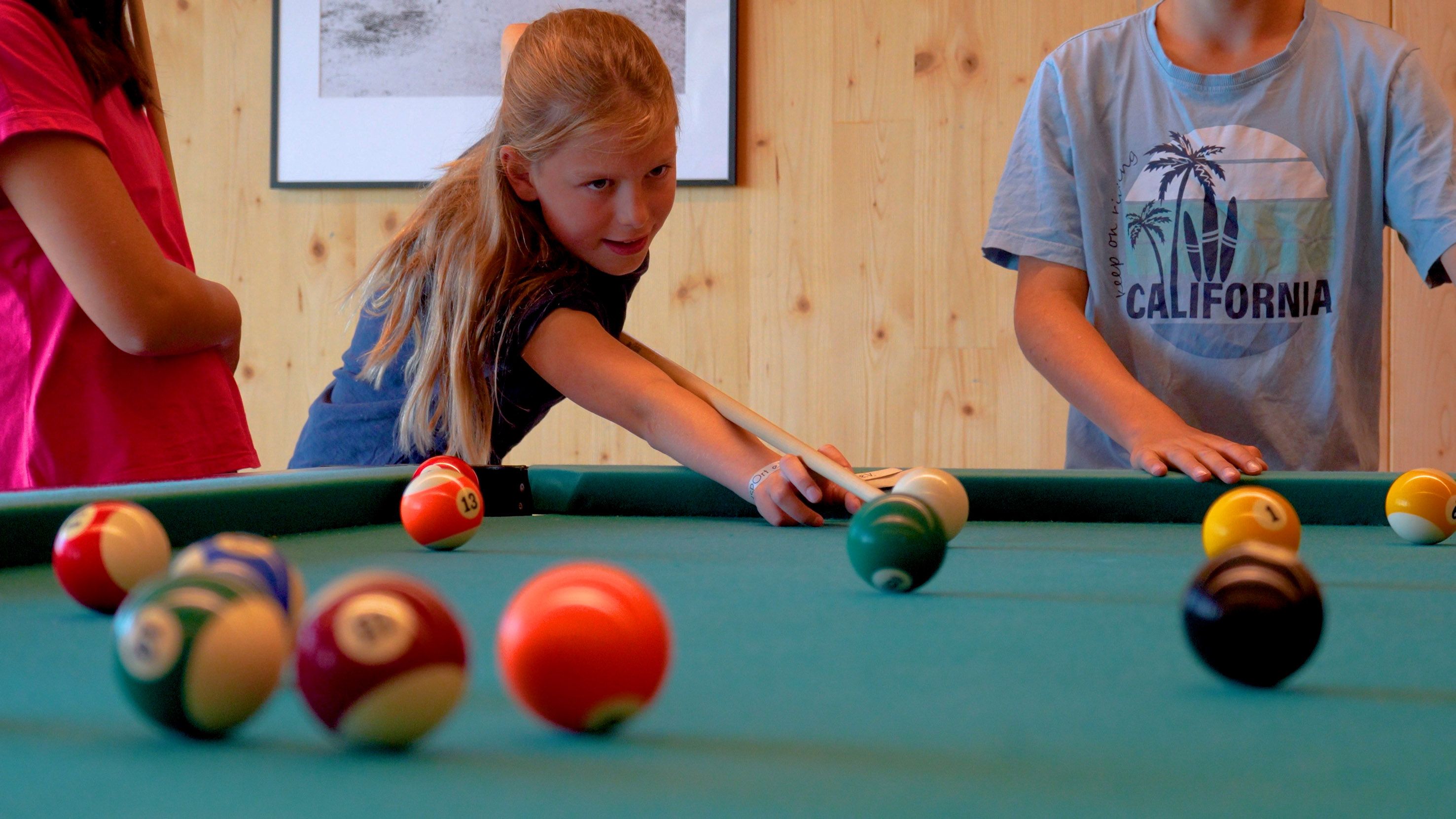 Drei Kinder, zwischen 8 und 12 Jahren, spielen Billiard. 