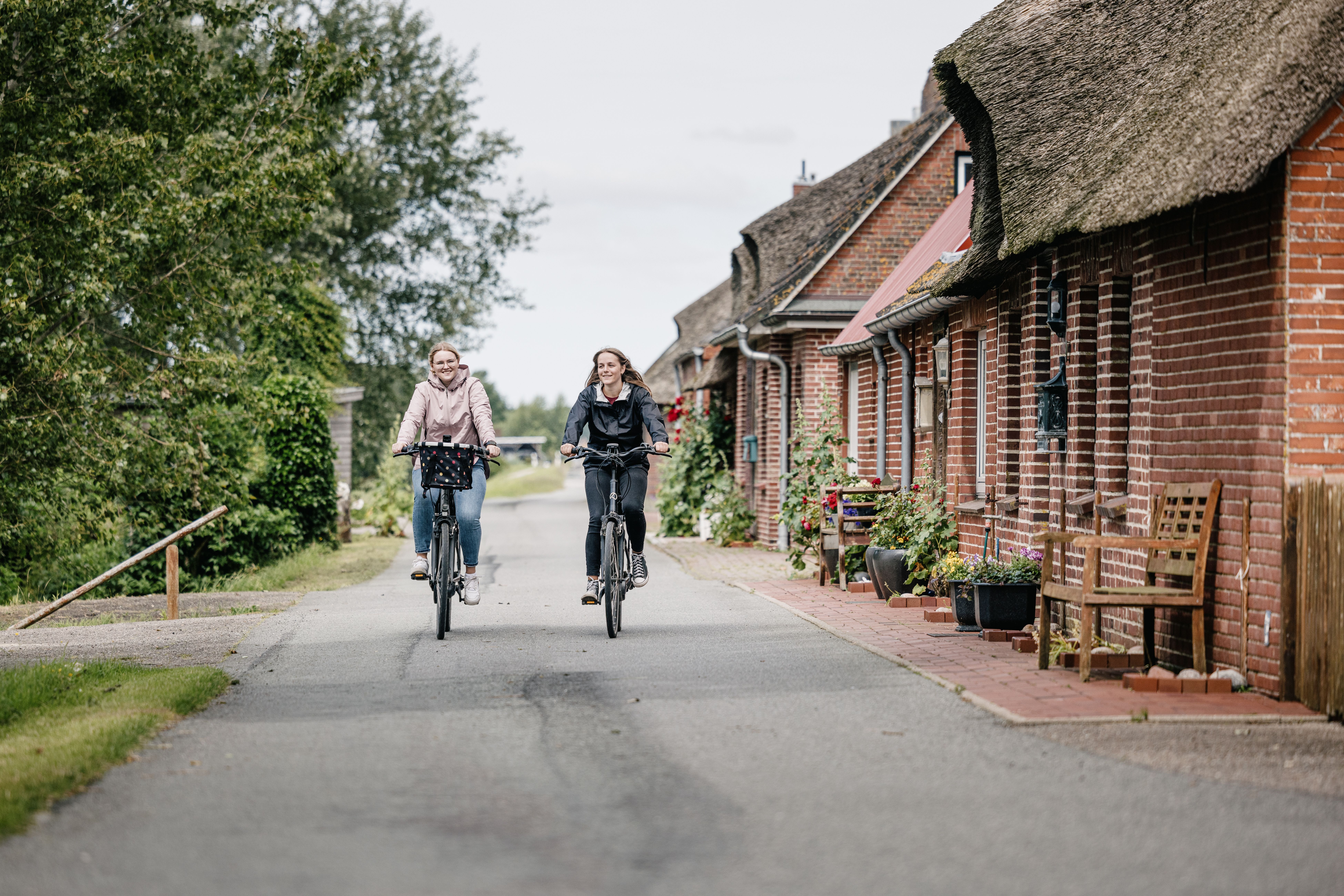 Zwei Frauen fahren mit ihren Fahrrädern auf einem alten Deich an dem Häuser stehen. Foto: Nordseeküste Nordfriesland | Markus Rohrbacher