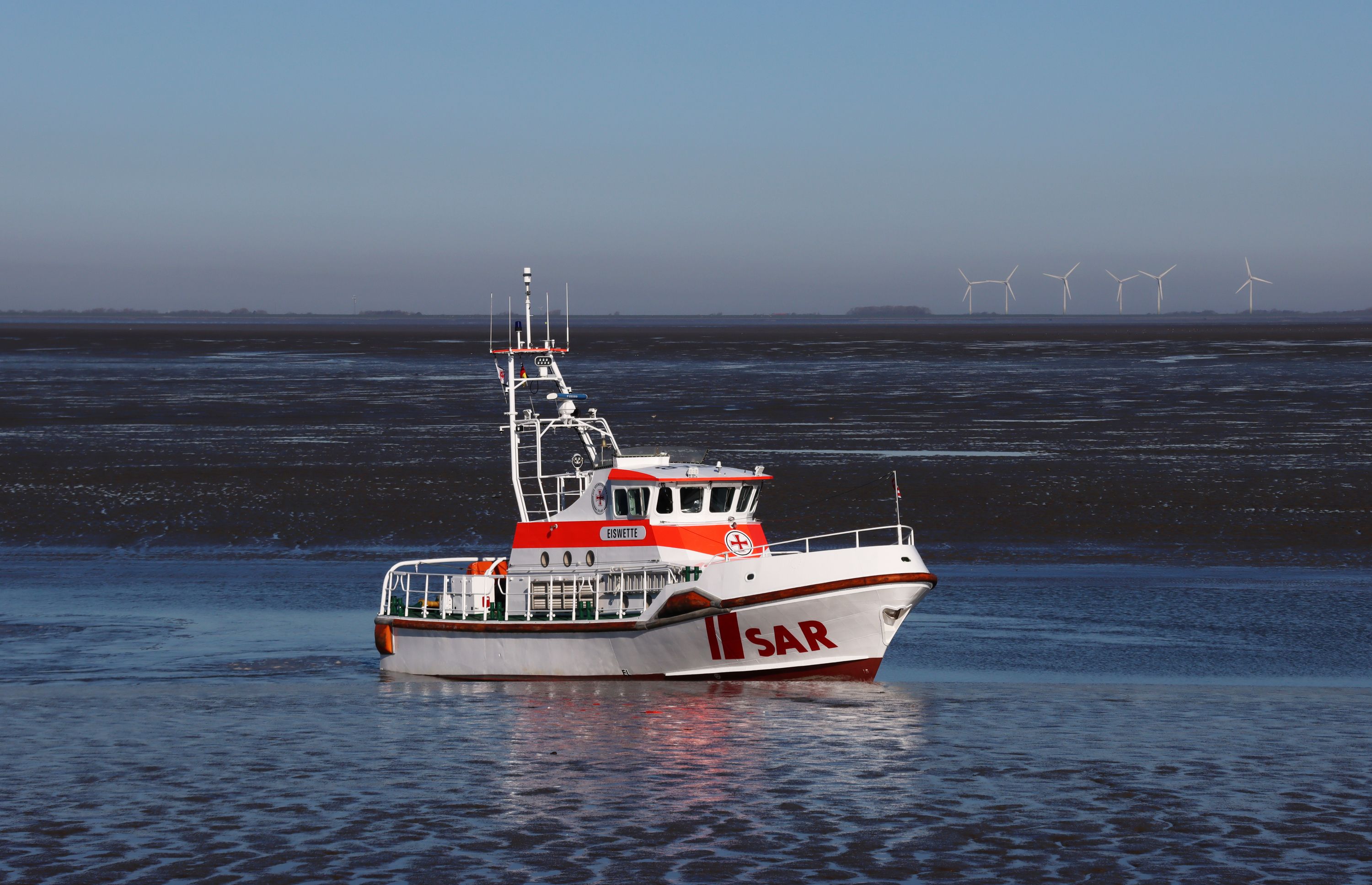 Der Seenotrettungskreutzer Eiswette fährt langsam durch die Fahrrinne bei Ebbe.
