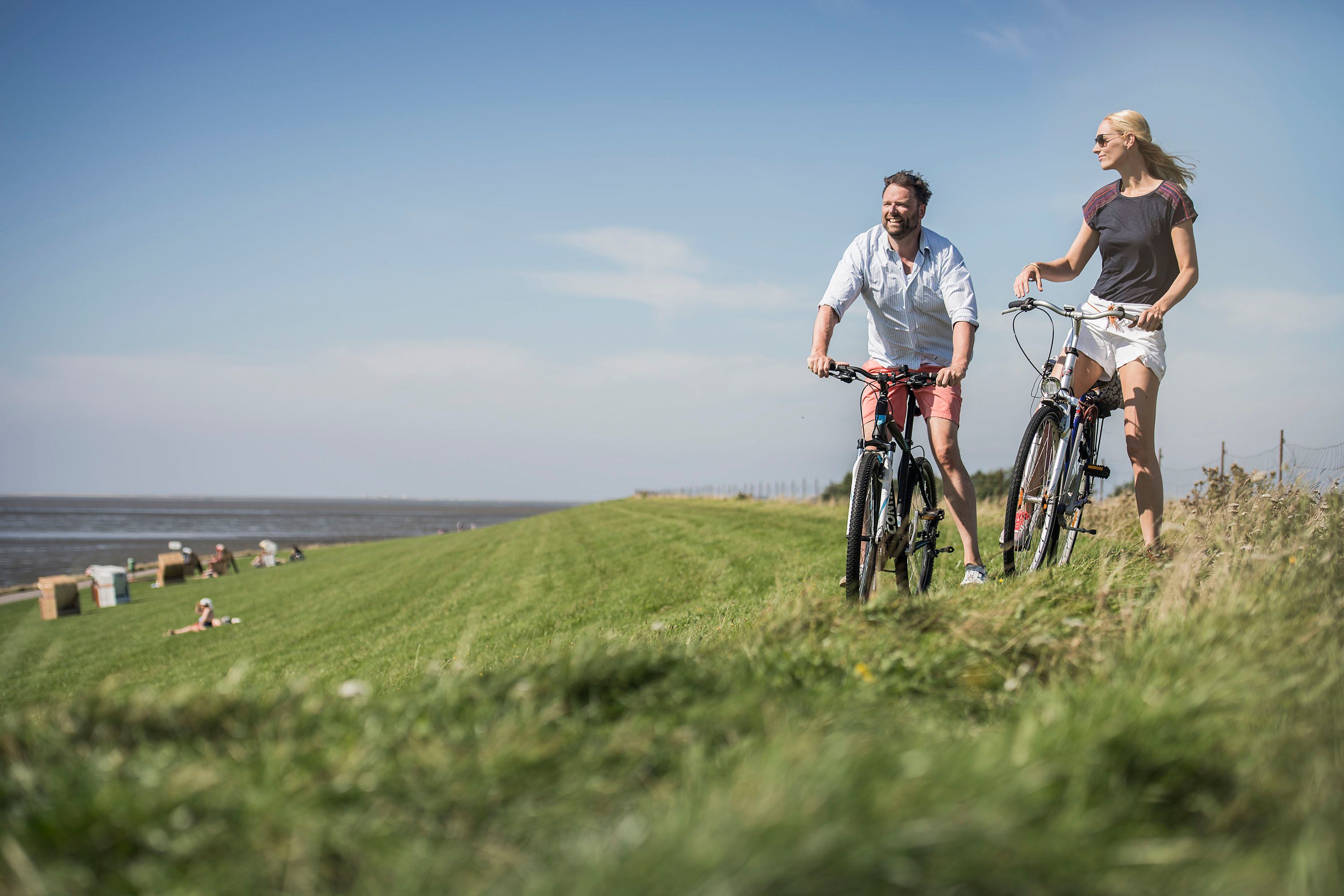 Eine Frau und ein Mann stehen mit ihren Fahrrädern im Sommer auf einem Deich