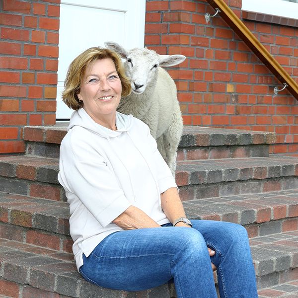 Autorin Dora Heldt sitzt auf Treppenstufen, neben ihr steht ein Schaf