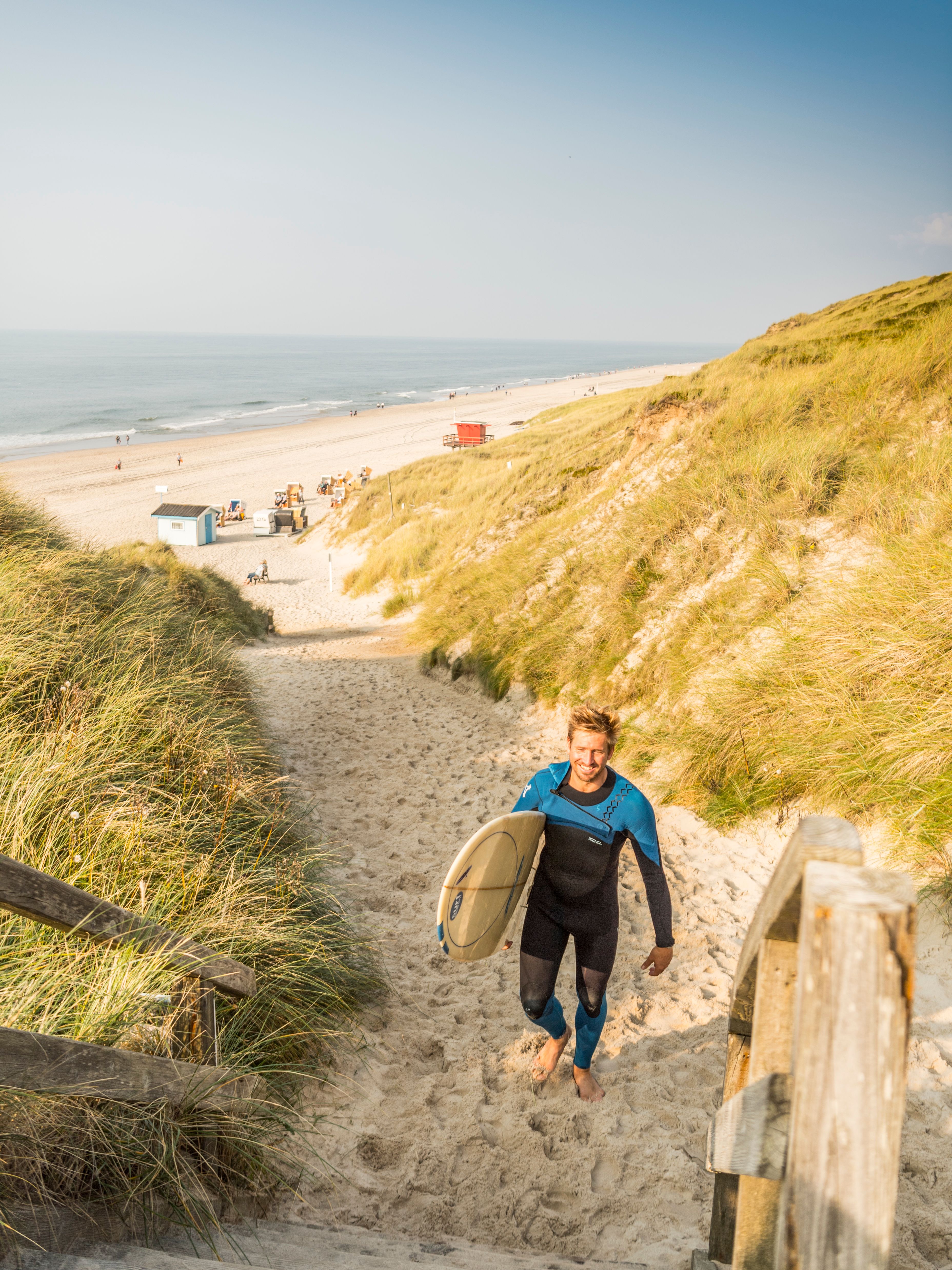 Ein hübscher Surfer trägt sein Brett am Strand von Wenningstedt auf Sylt.
