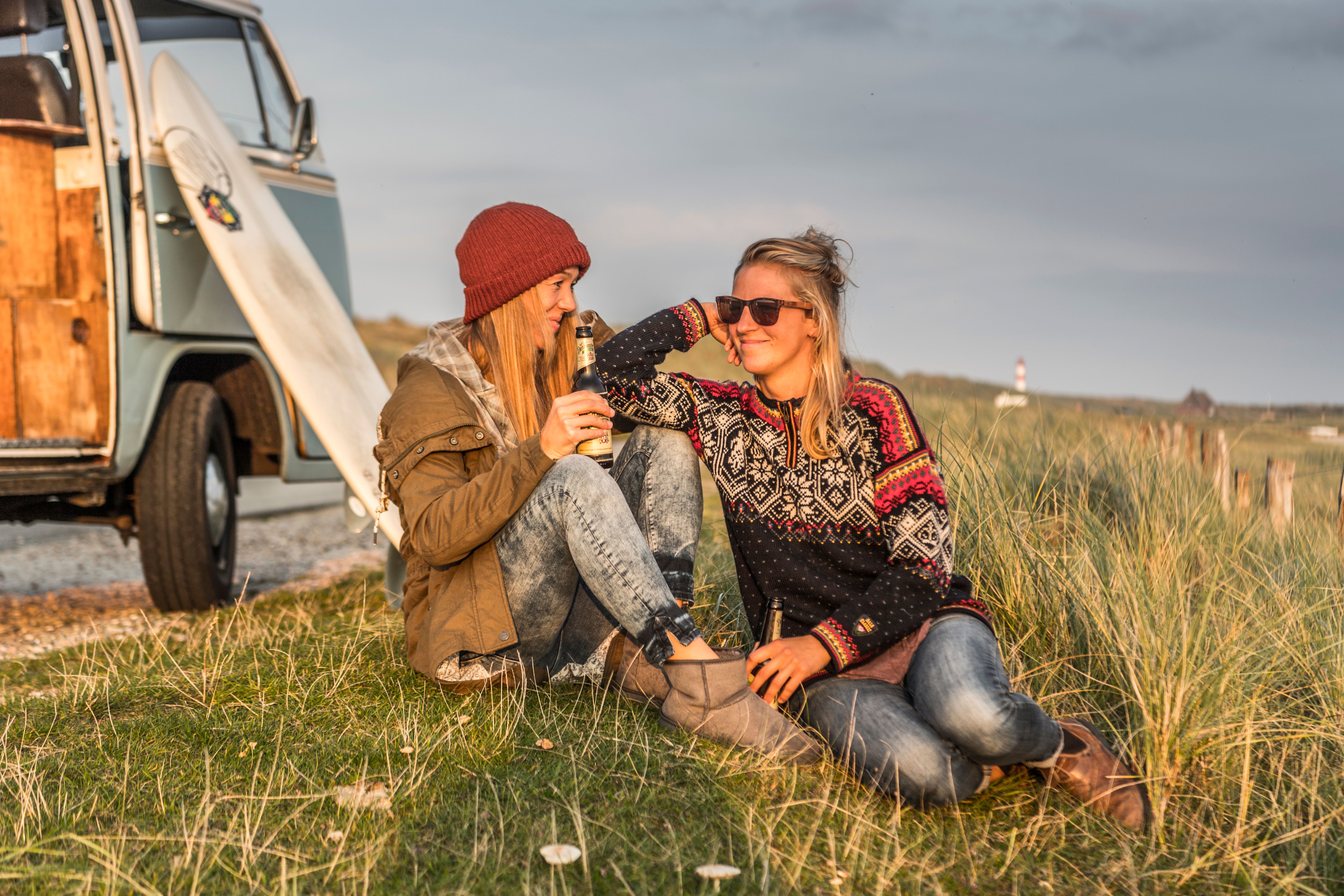 Beim Camping an der Nordsee genießen zwei Mädchen ein Bier beim Sonnenuntergang. 