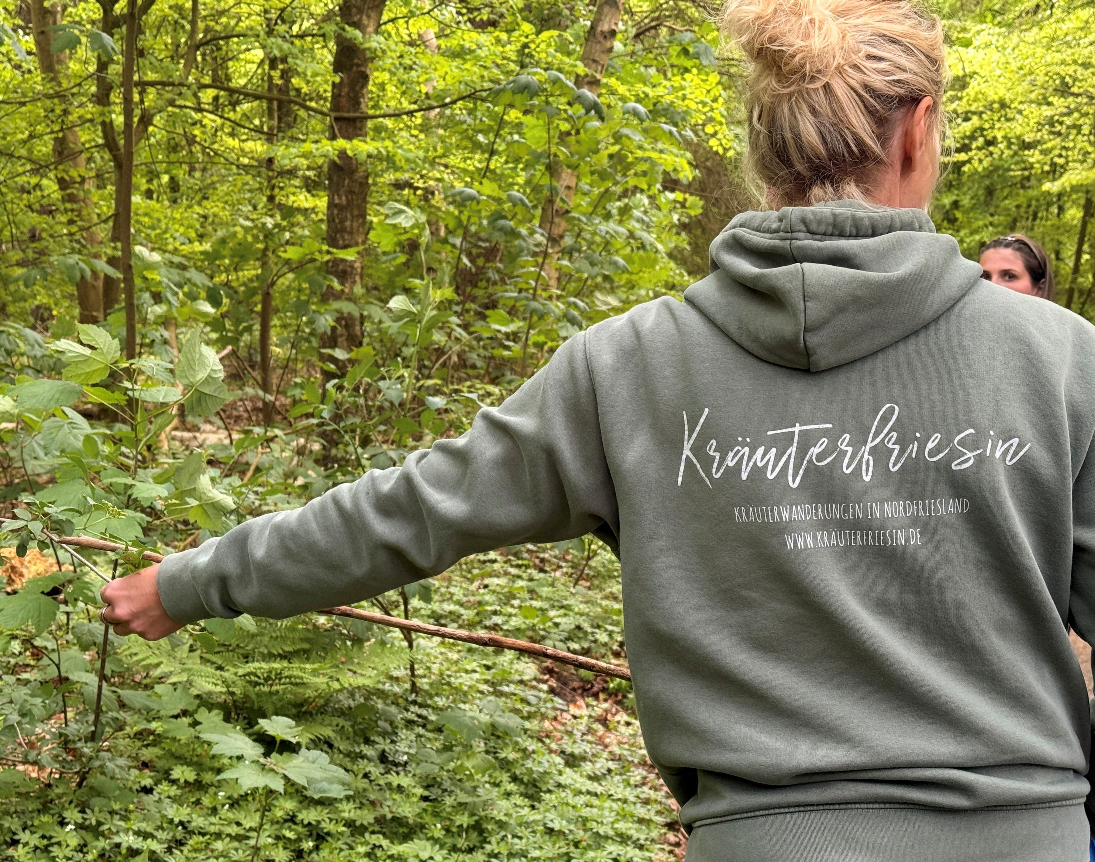 Die Kräuterfriesin zeigt Teilnehmenden der Kräuterwanderung Kräuter, die man im Wald findet und deutet darauf. Foto: Inga Lorenzen