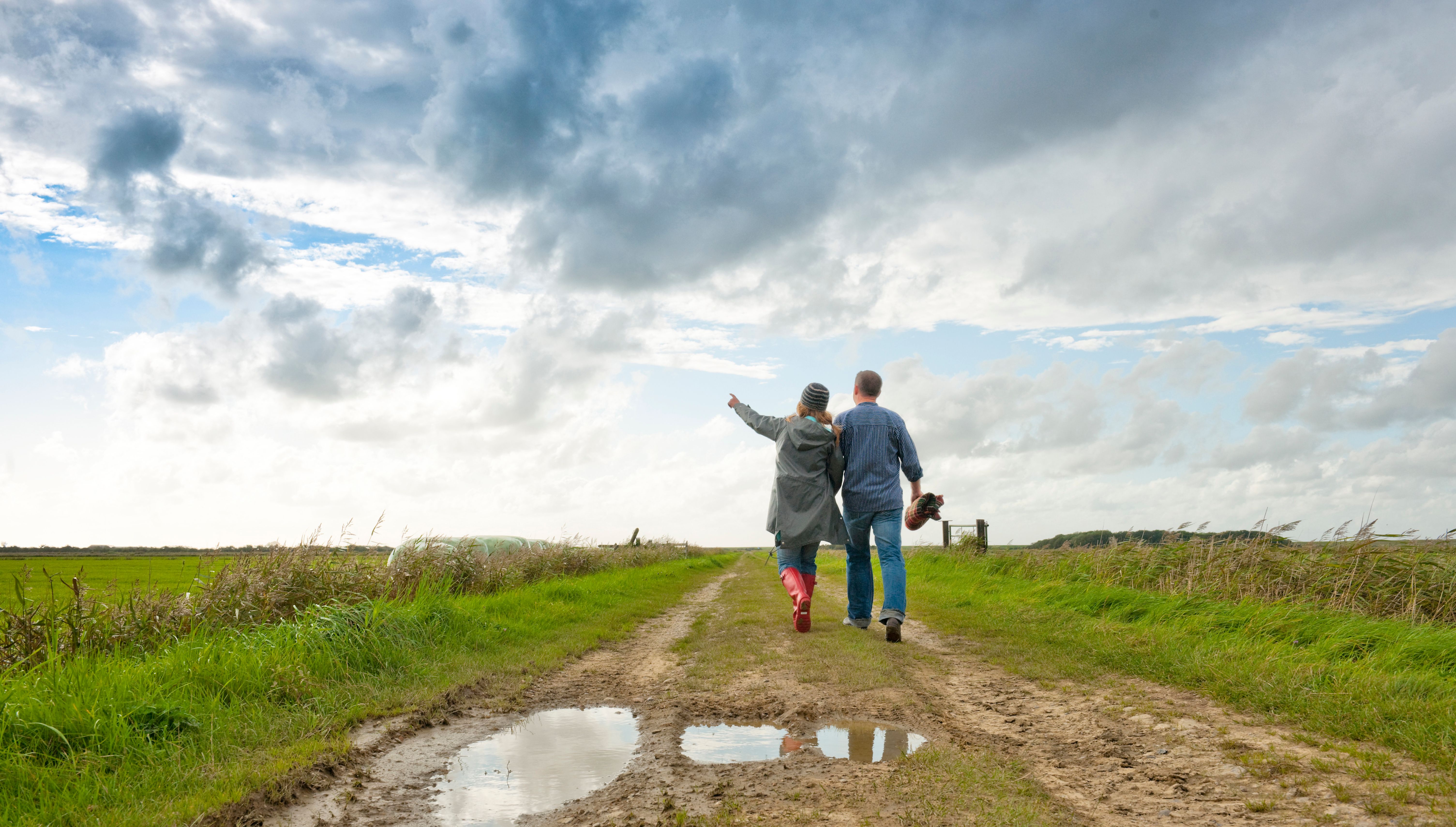 Ein Paar wandert über einen Feldweg hinaus in die Föhrer Marschenlandschaft – Foto: Föhr Tourismus GmbH | Oliver Franke
