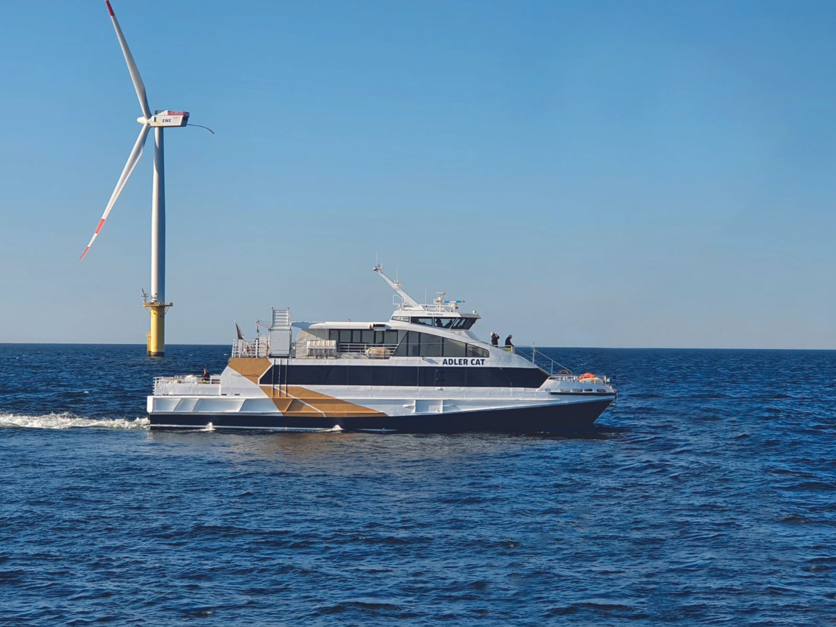 Die Adler Cat fährt vor einem Windpark her